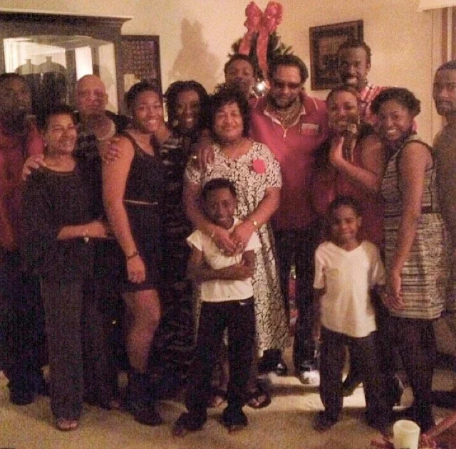 Large family group posing in a warmly decorated room, possibly during a holiday gathering or special occasion, with Christmas decorations visible in the background.