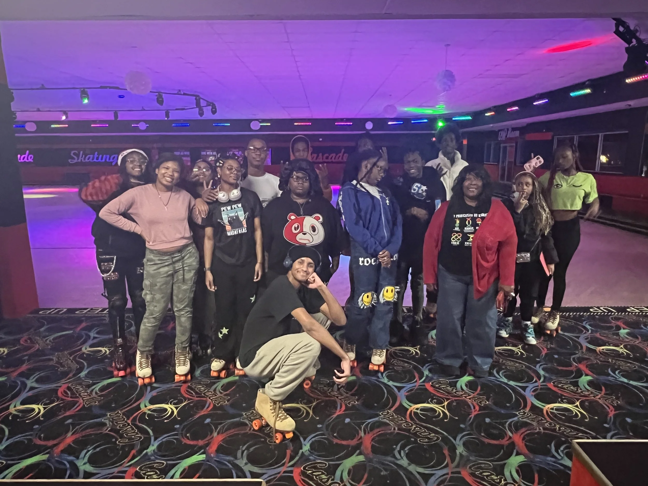 Group of people wearing roller skates at an indoor roller skating rink with colorful lights and patterns on the floor.