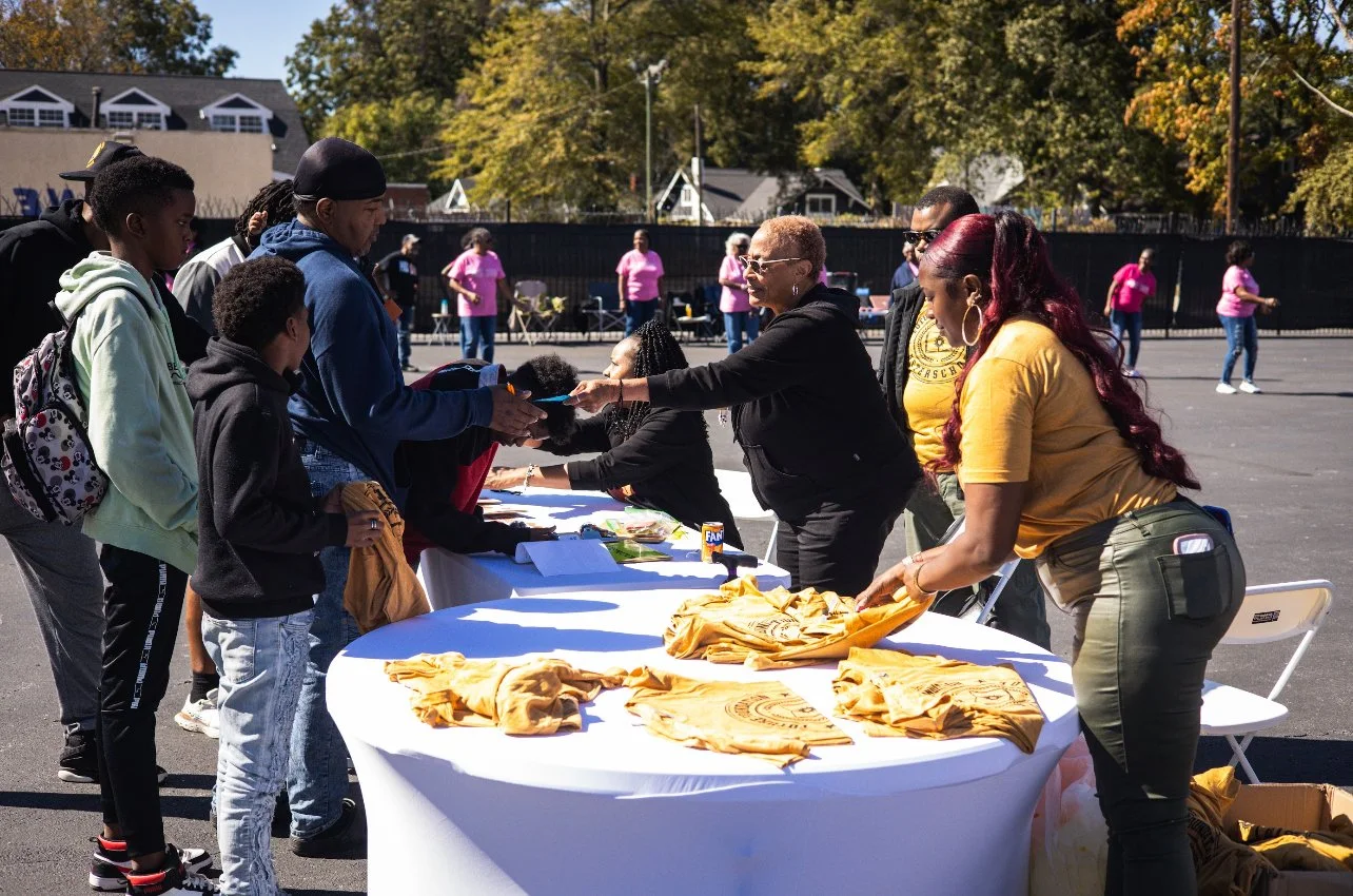 People gathered at an outdoor event, signing up at tables with yellow T-shirts.
