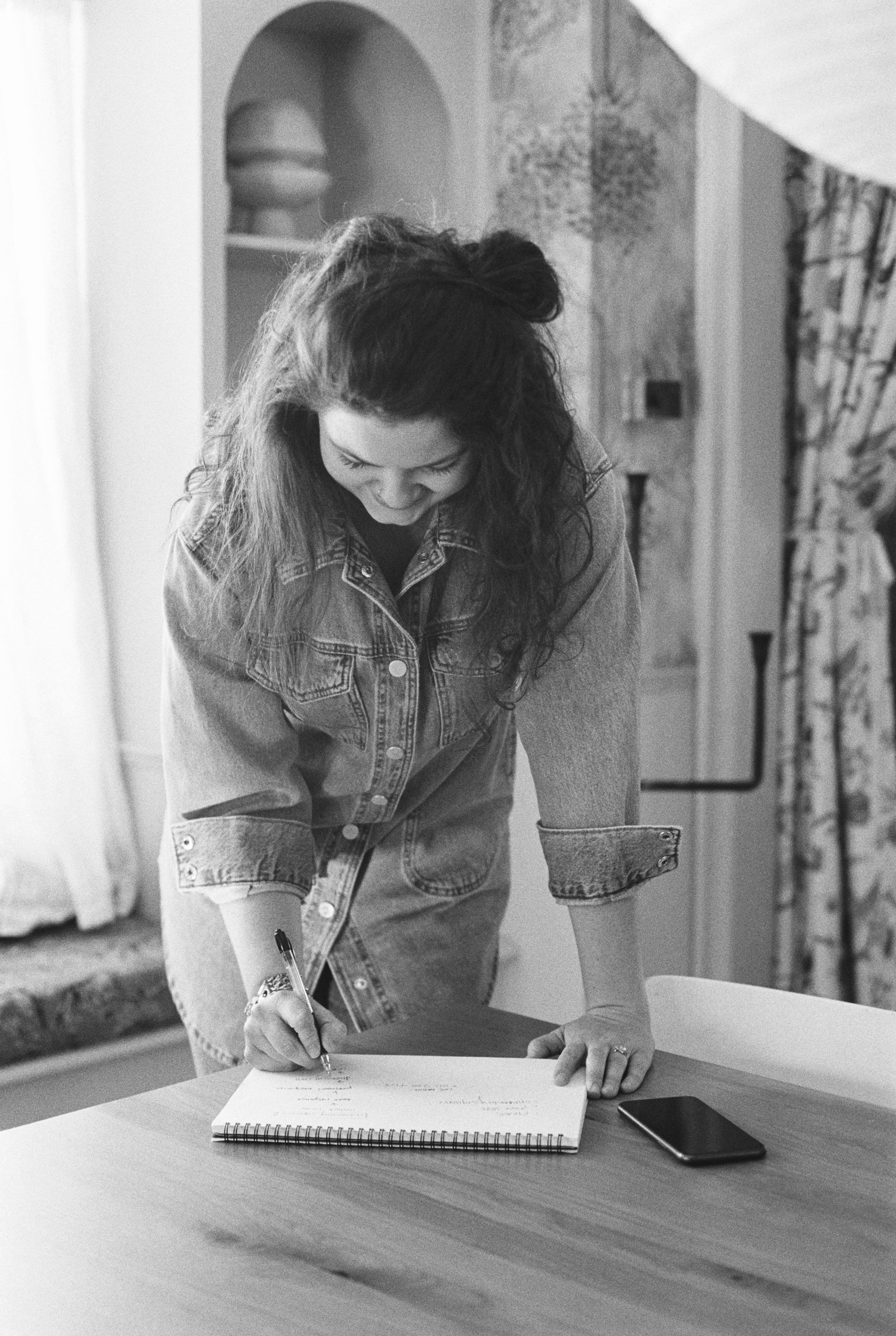Black and white image of a creative professional writing notes at a table, symbolizing the client offboarding process for photographers and how to create a polished, professional client experience that encourages referrals.