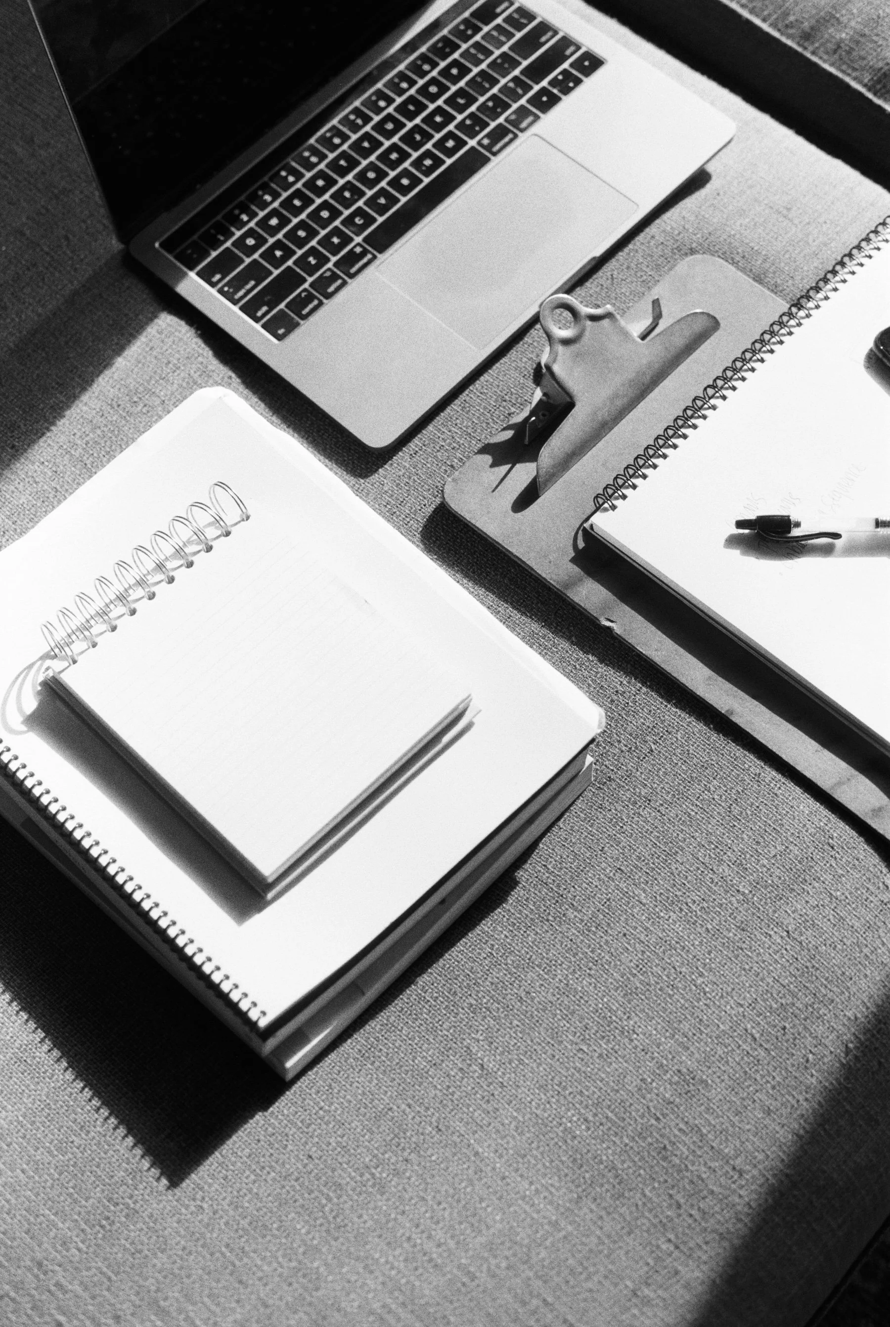Black and white photo of a photographer organizing their workspace with a laptop, notebooks, and a clipboard, reviewing client inquiries and streamlining their workflow to prevent missed photography leads.