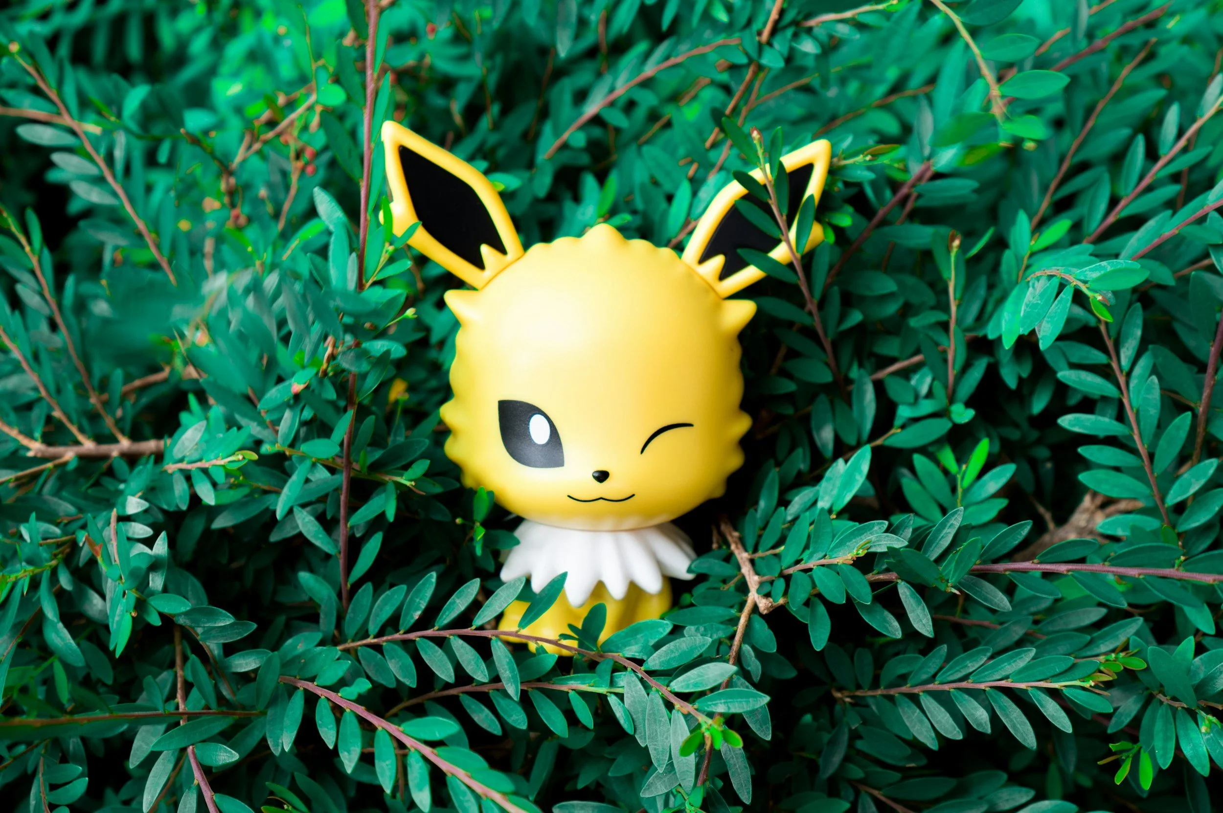 Jolteon figurine winking in green foliage.