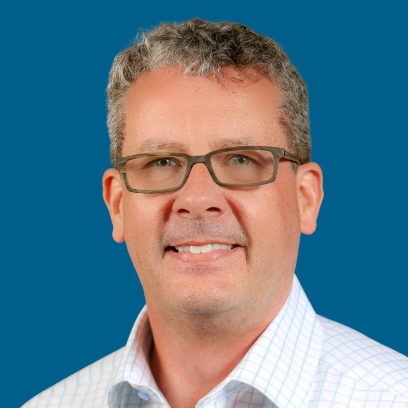 Kevin Kruse smiling in glasses against a blue background, leadership speaker and author