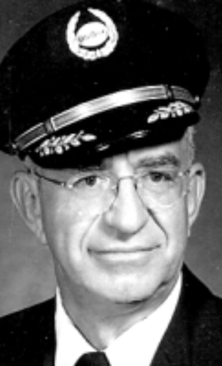 Black-and-white portrait of a man in a formal military uniform, wearing glasses and a hat with an emblem.