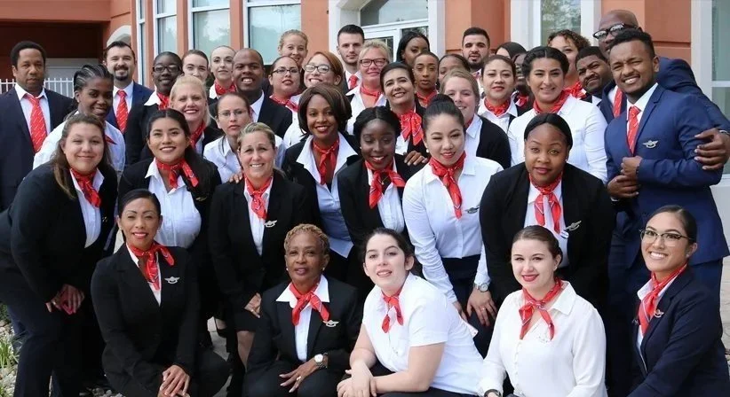 Group of diverse airline employees in uniform, smiling outside a building.
