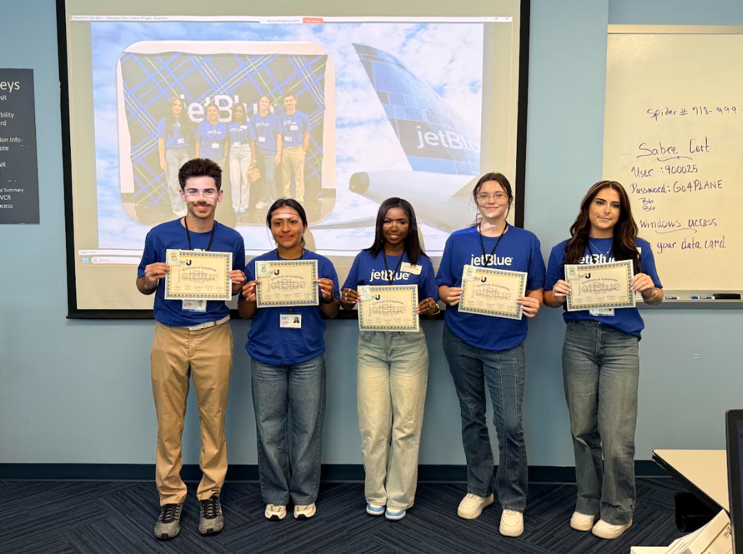 Five young people standing in a classroom, holding certificates and smiling, with a projection screen in the background displaying a group photo at a JetBlue event.