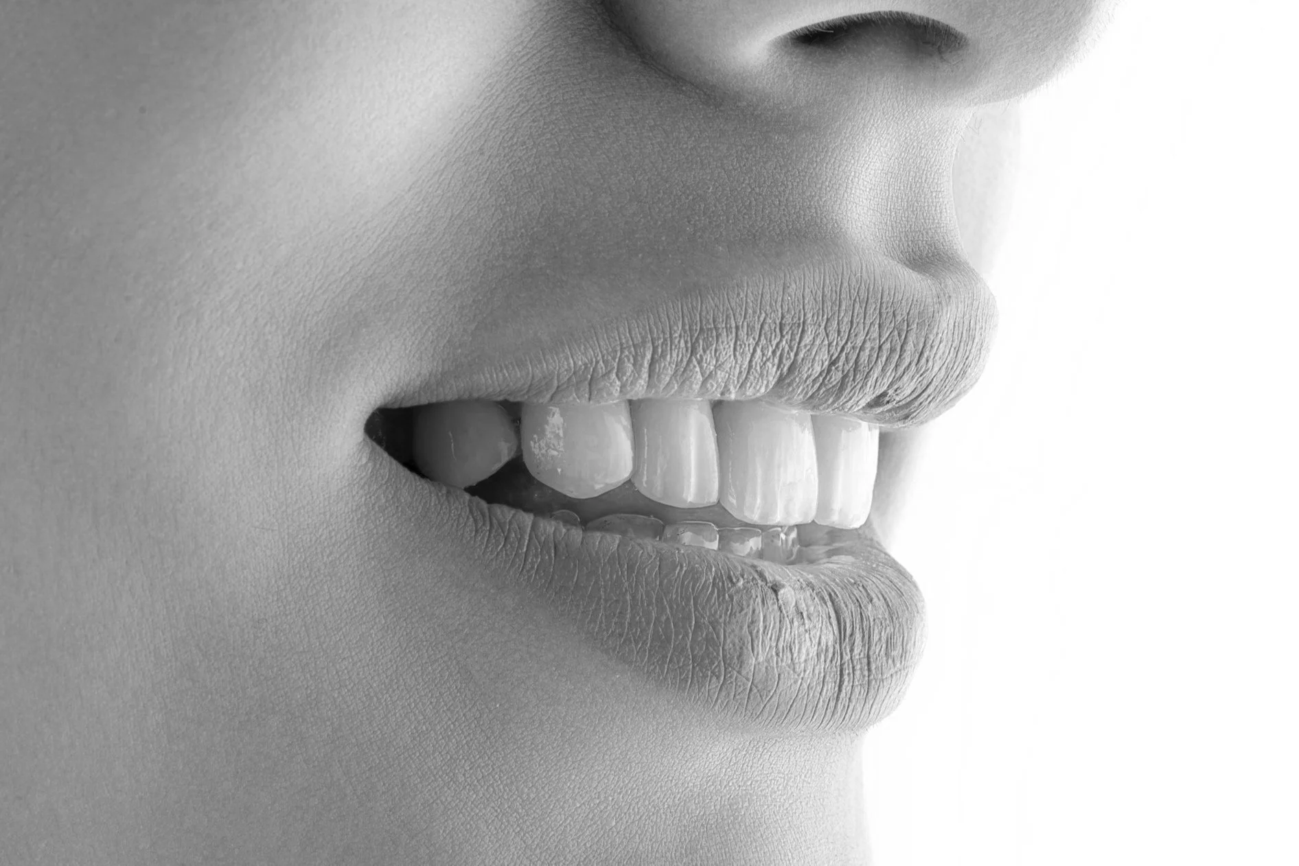 Close-up of a person's mouth slightly open, showing teeth and lips in black and white.