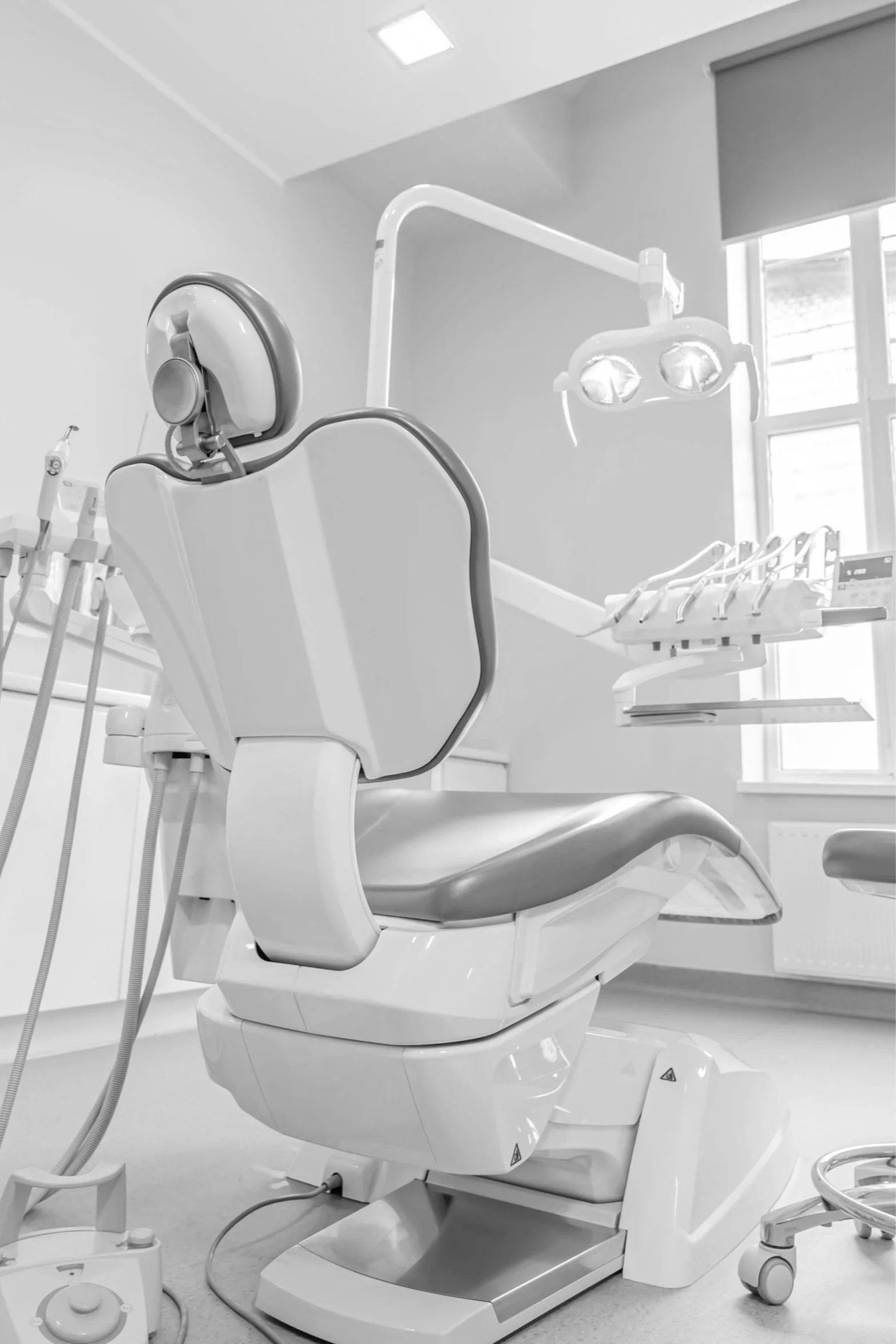 A dental examination chair in a clean, well-lit dental clinic with dental equipment and overhead lights.