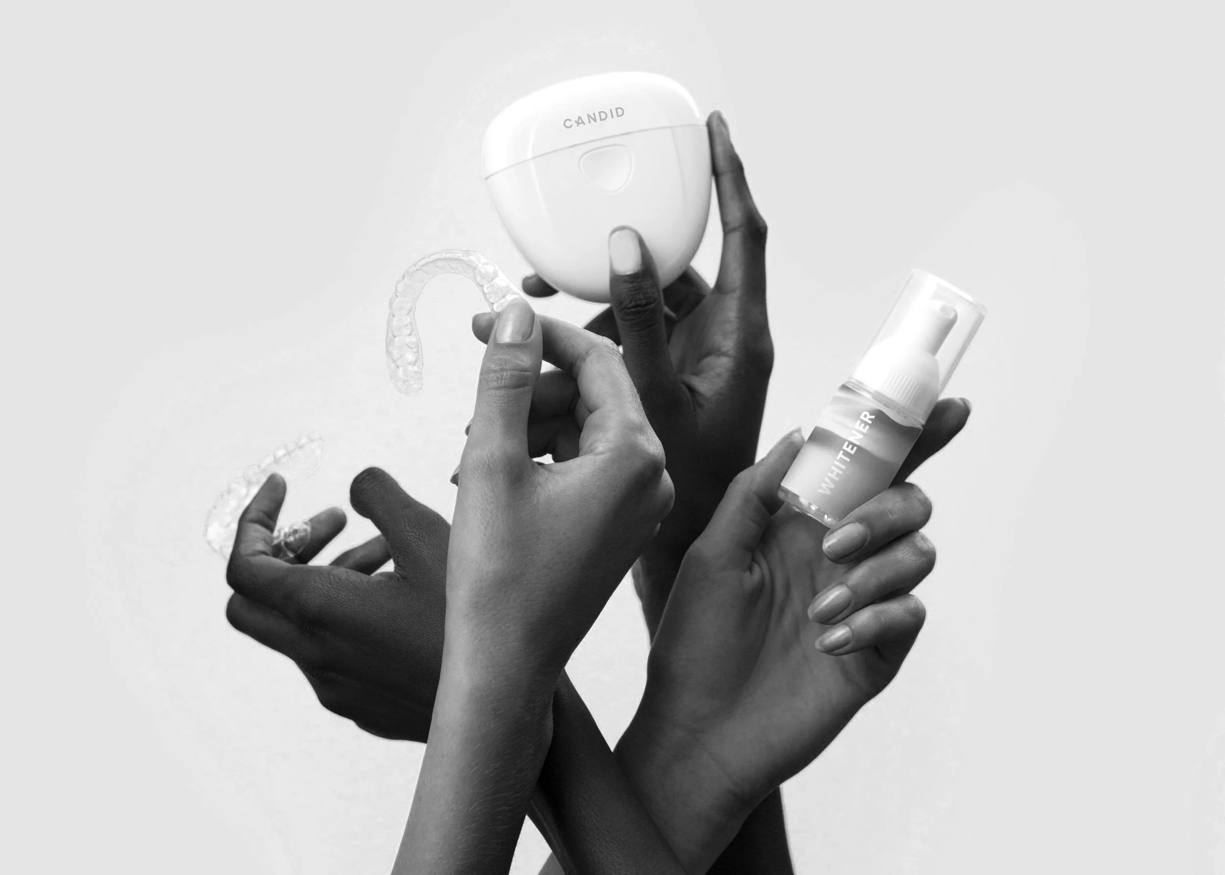 Multiple hands holding dental and teeth whitening products, including mouth guards and a spray bottle labeled 'WHITENER', against a plain background.