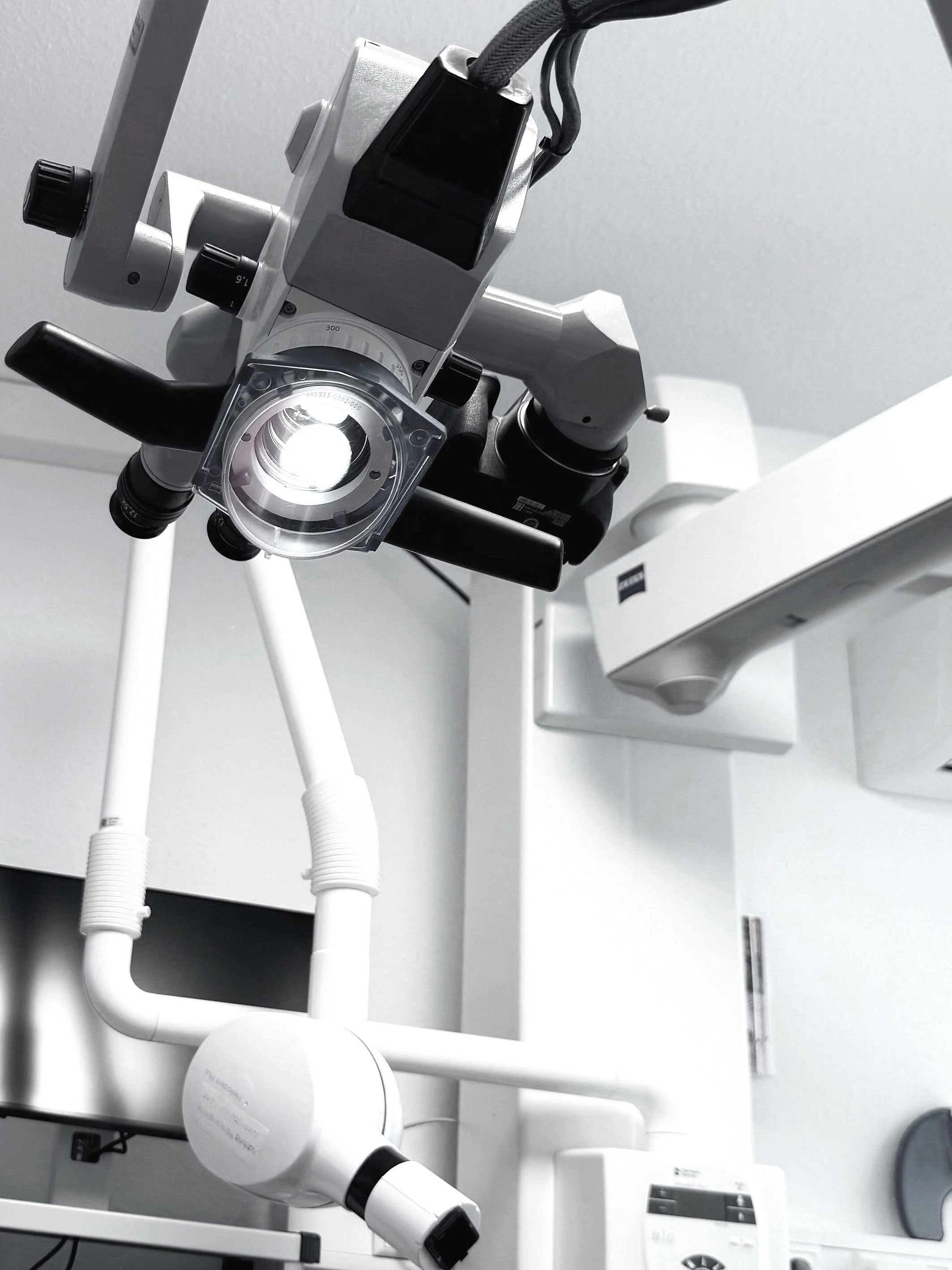 A close-up view of a medical or dental examination microscope mounted on a wall, with various connected parts and controls.