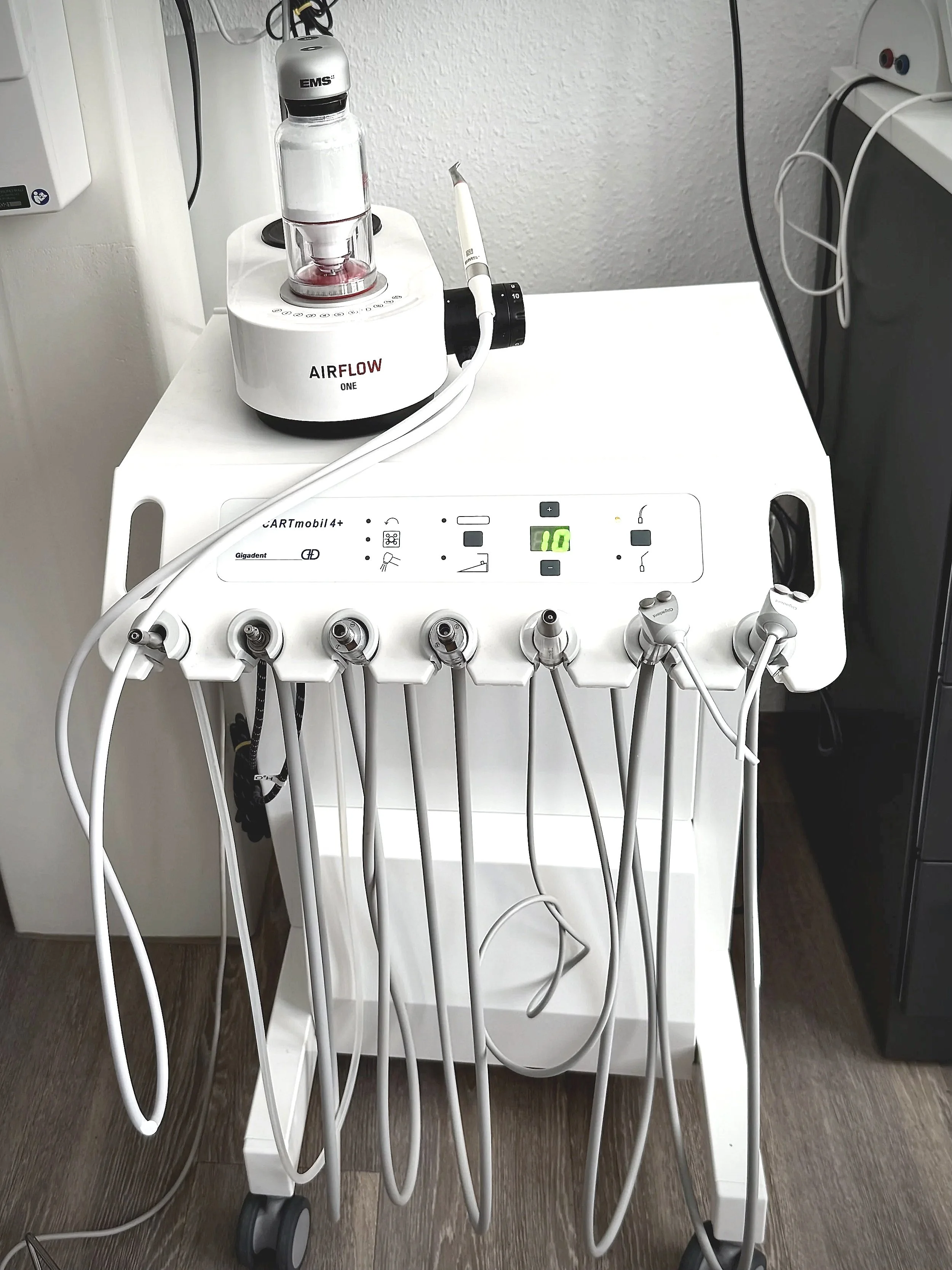 Dental suction equipment with multiple handpieces and tubing on a white cart in a dental clinic.