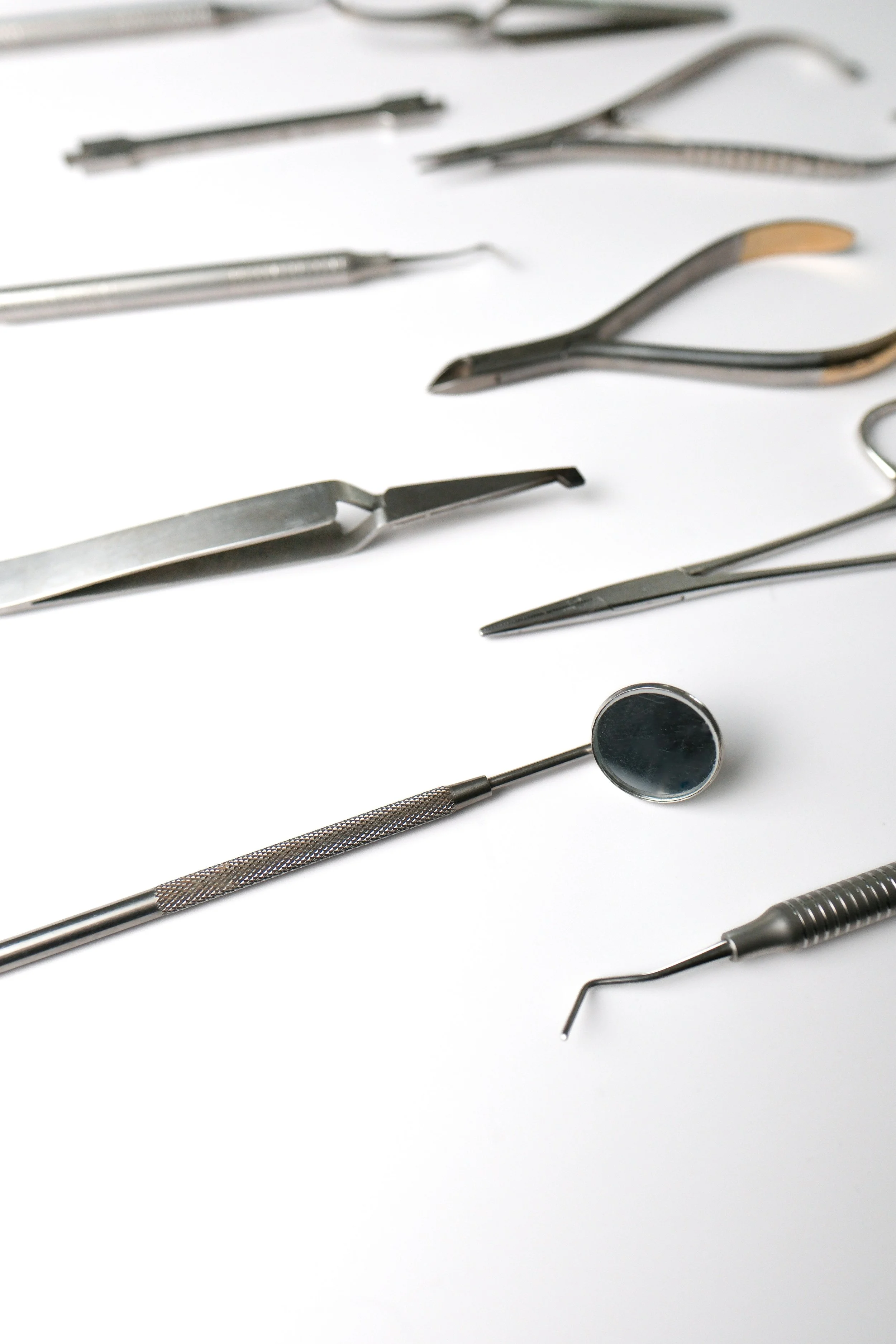 Dental tools including a mirror, probes, and other instruments laid out on a white surface.
