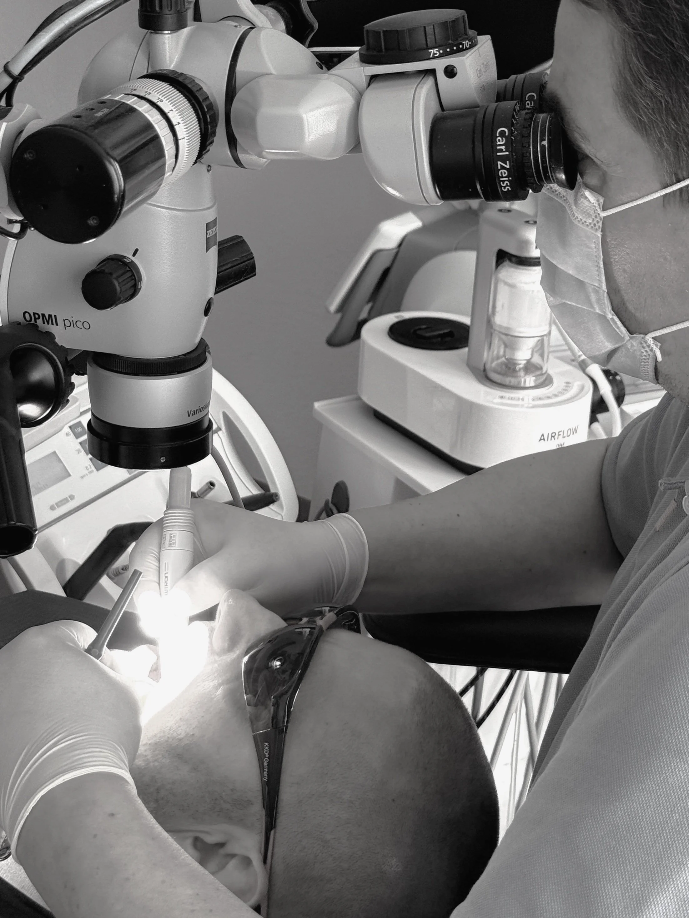 A scientist performing surgery or a procedure using a microscope, wearing gloves, a face mask, and protective glasses, in a laboratory setting.