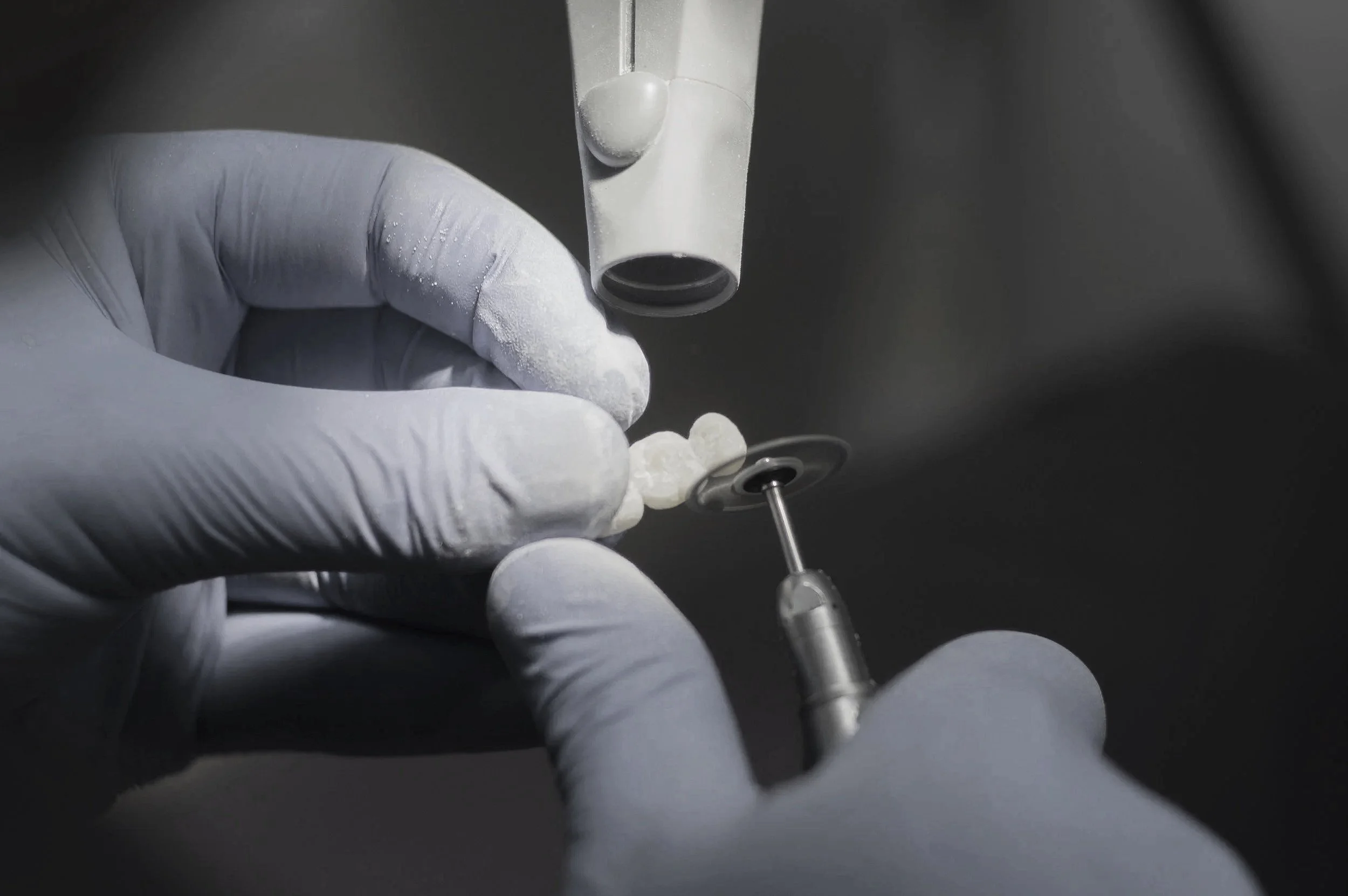 Dentist wearing gloves uses a dental handpiece to treat a tooth under an overhead dental microscope.