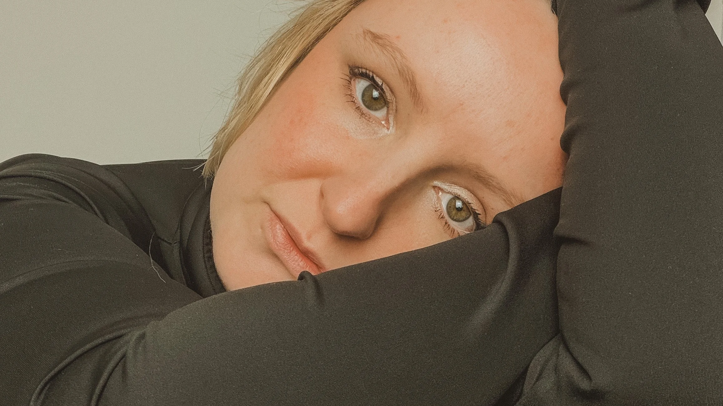 fine artist  portrait of Emma Cawston with green eyes and light makeup, resting her head on her arm, wearing a black jacket.