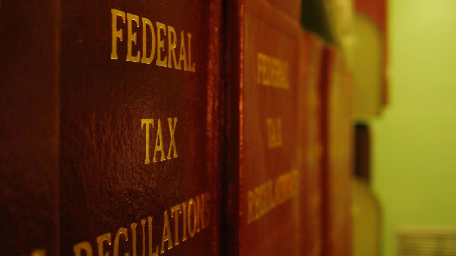 A row of red legal books organized on a shelf, with gold lettering on the spine reading 'Federal Tax Regulation'.