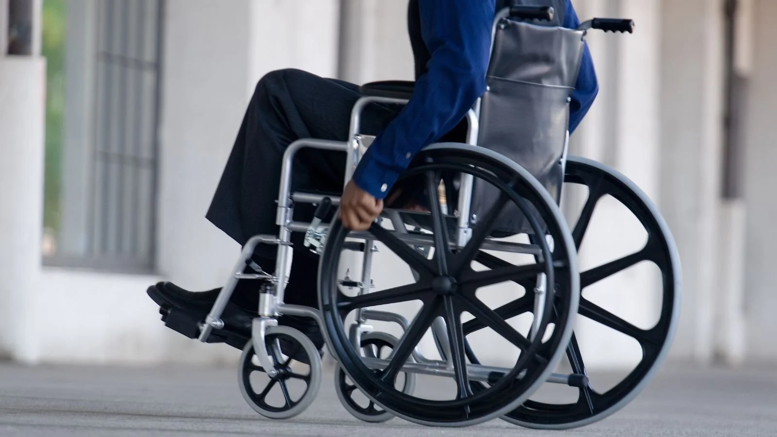 Person in a wheelchair moving forward outdoors, wearing a blue shirt.