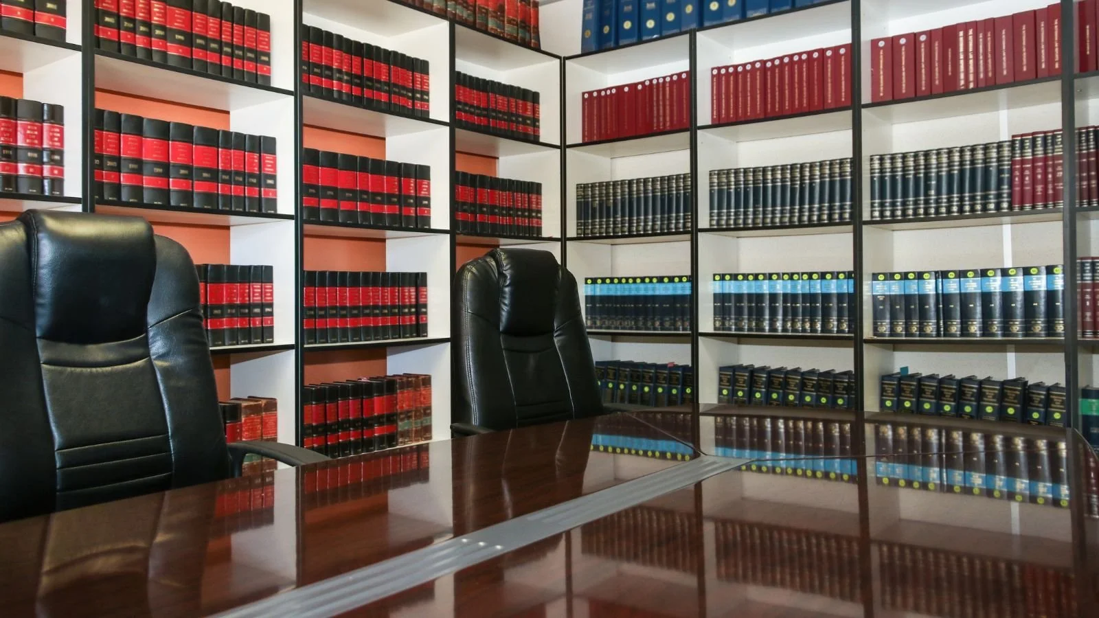 Interior of a law office or library with black leather chairs, a wooden conference table, and shelves filled with legal books.