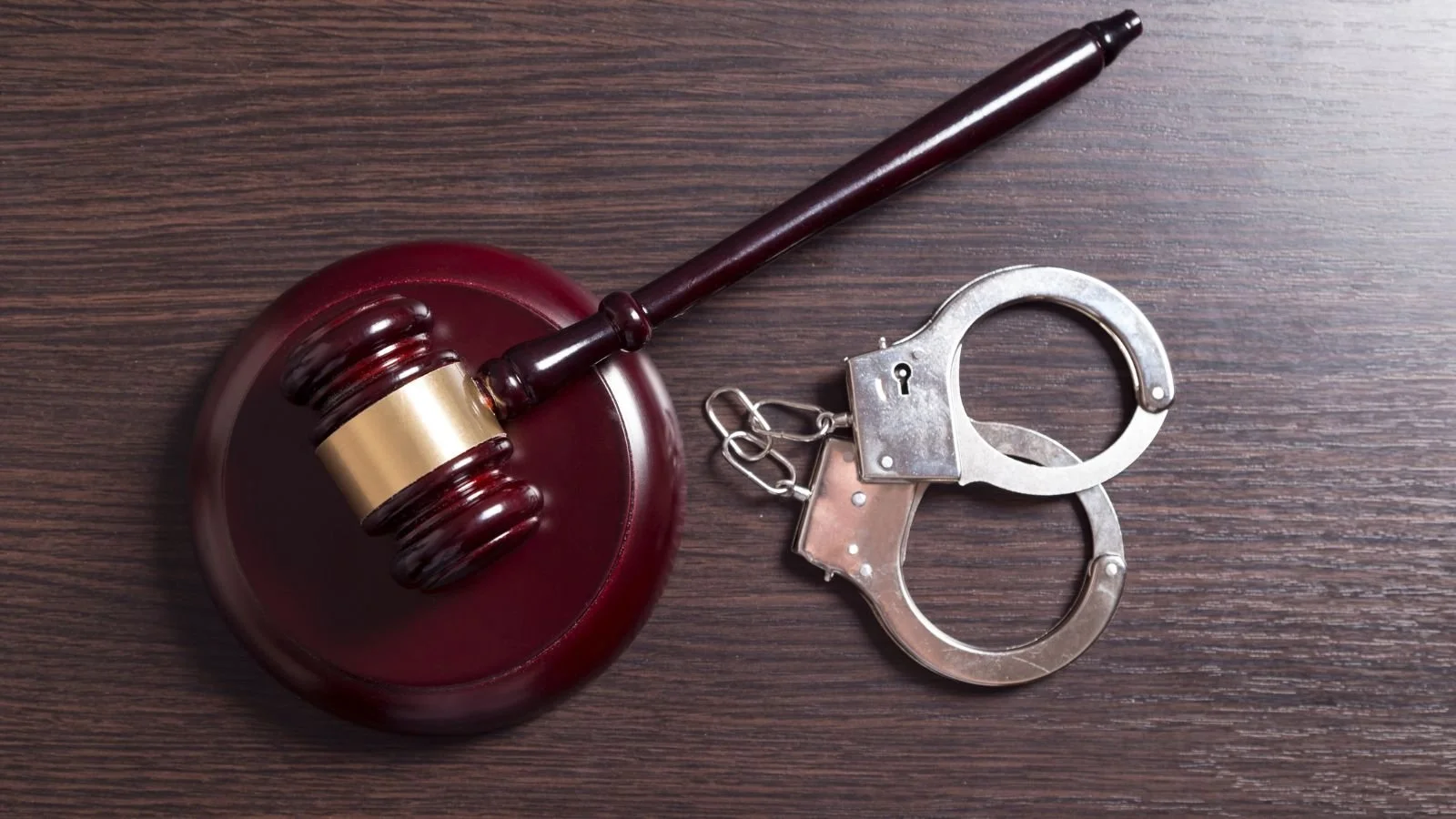 A judge's gavel and a pair of handcuffs on a wooden surface.