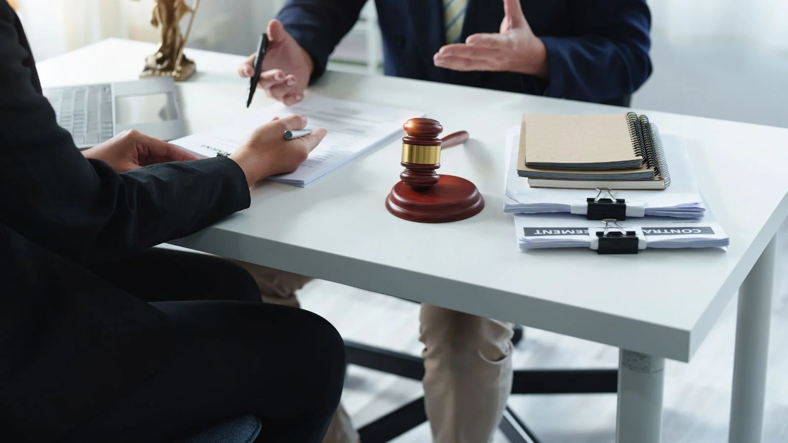 A legal or courtroom setting with a judge's gavel on the desk, a person signing documents, and another person gesturing while discussing.