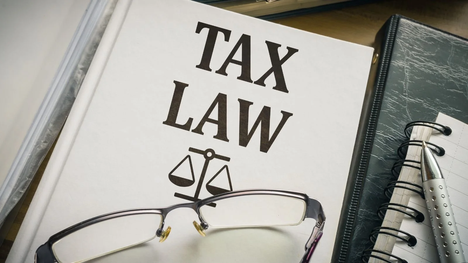 Legal books titled 'Tax Law' with a pair of glasses, a planner, and a pen on a desk.