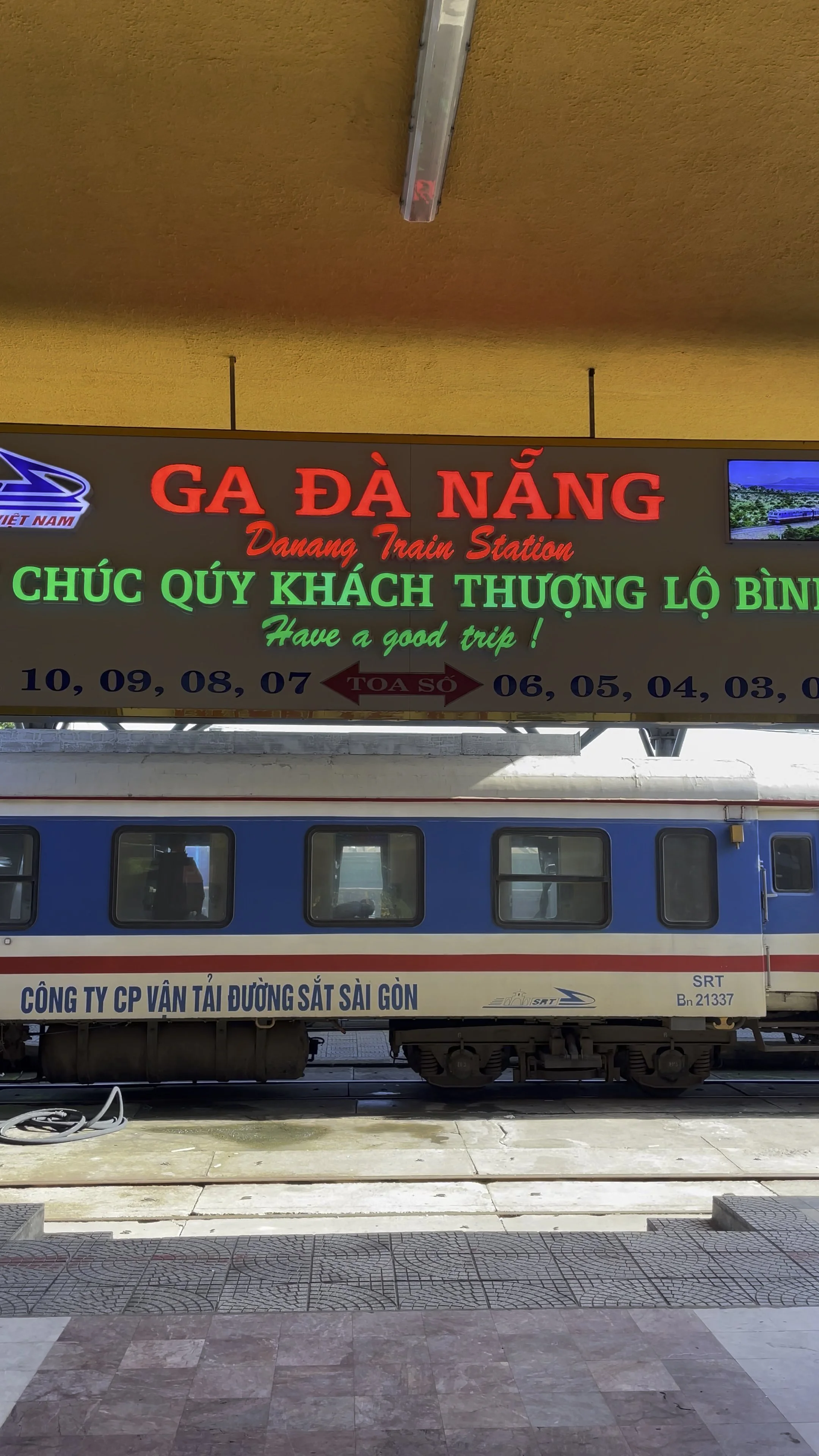 Sign for Da Nang train station in Vietnam with train below and text in Vietnamese and English, including platform numbers and company name in Vietnamese.