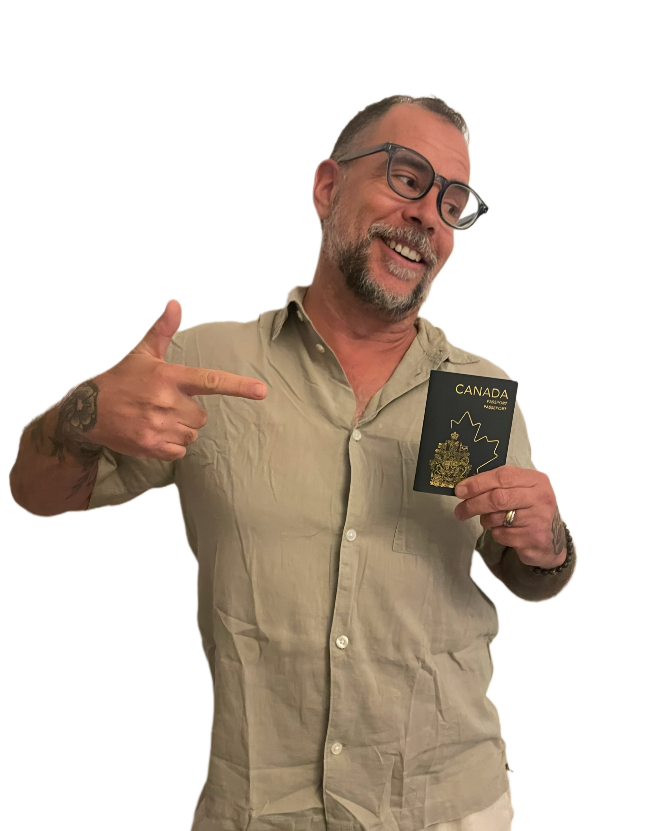 A man smiling and pointing at a Canadian passport he is holding, wearing glasses and a beige button-up shirt.