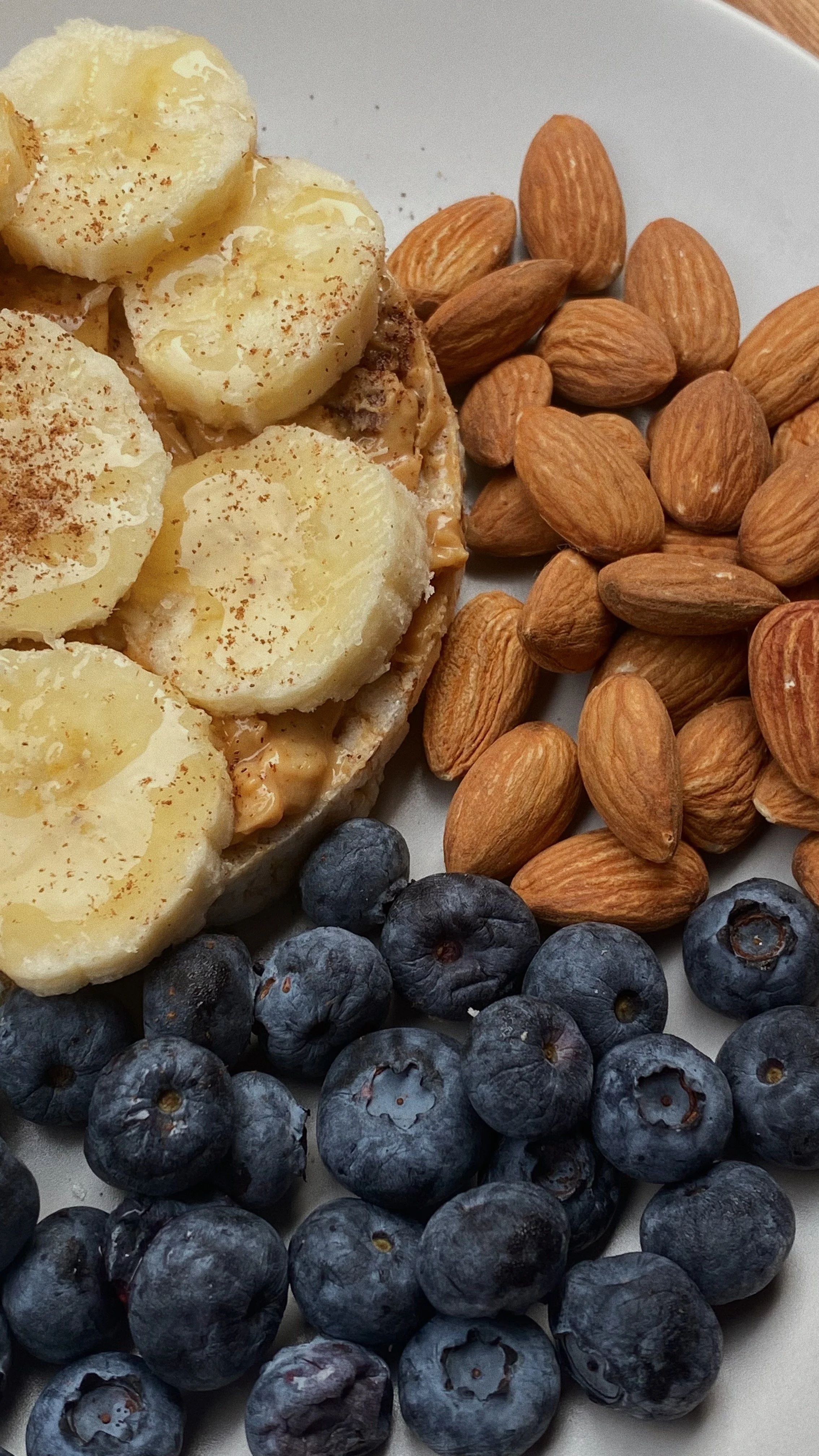 Sliced bananas with cinnamon on top, surrounded by almonds and blueberries on a white plate