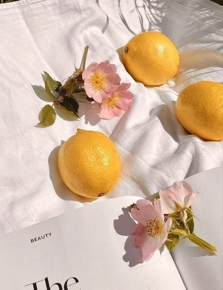Three lemons, a pink flower, and an open magazine on white fabric.