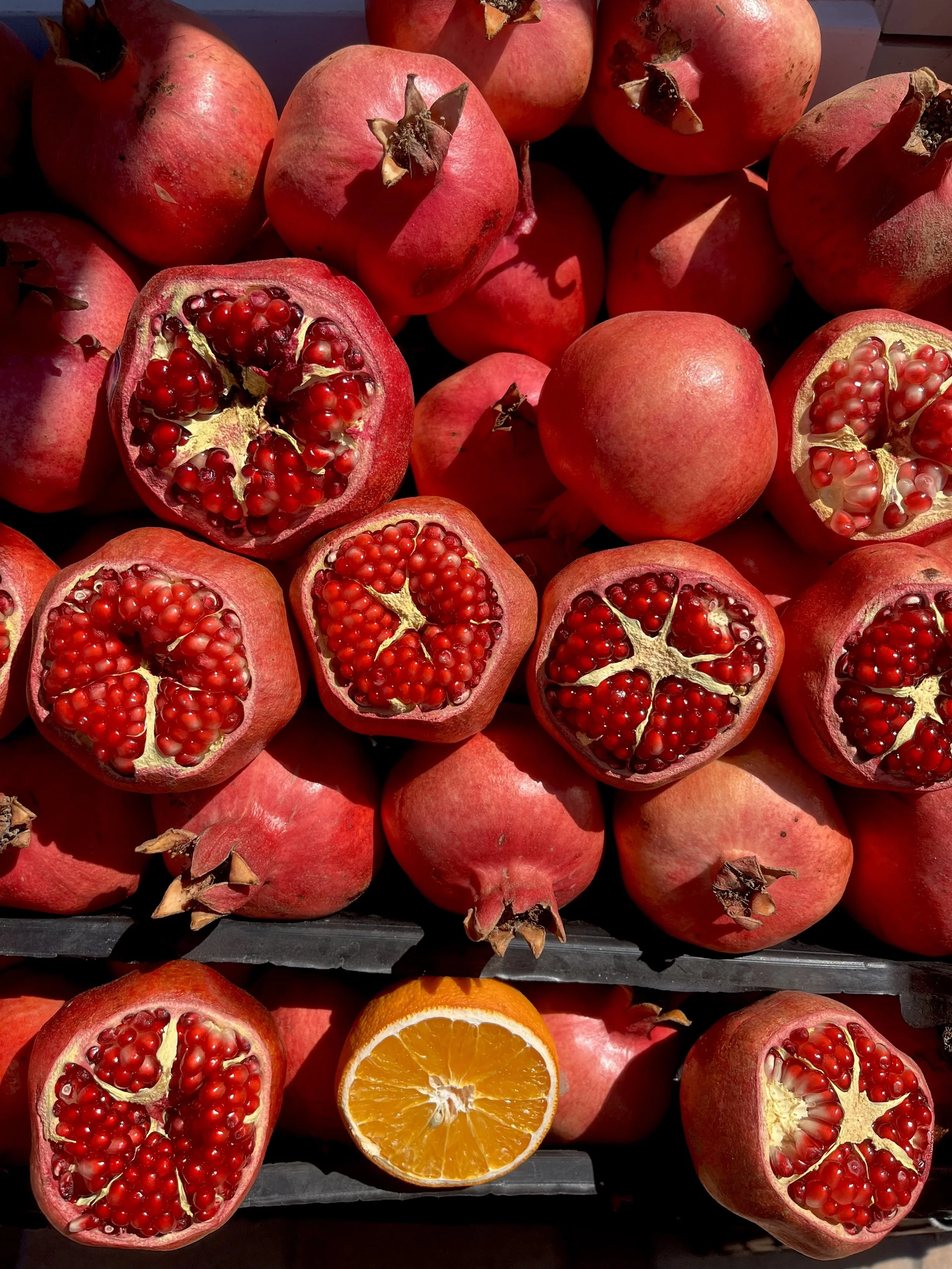 Pomegranate and orange fruits on display, with the pomegranates split open showing red seeds.