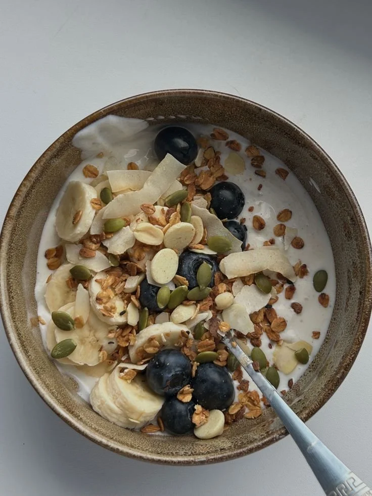 Bowl of yogurt topped with blueberries, sliced bananas, shredded coconut, granola, and pumpkin seeds.
