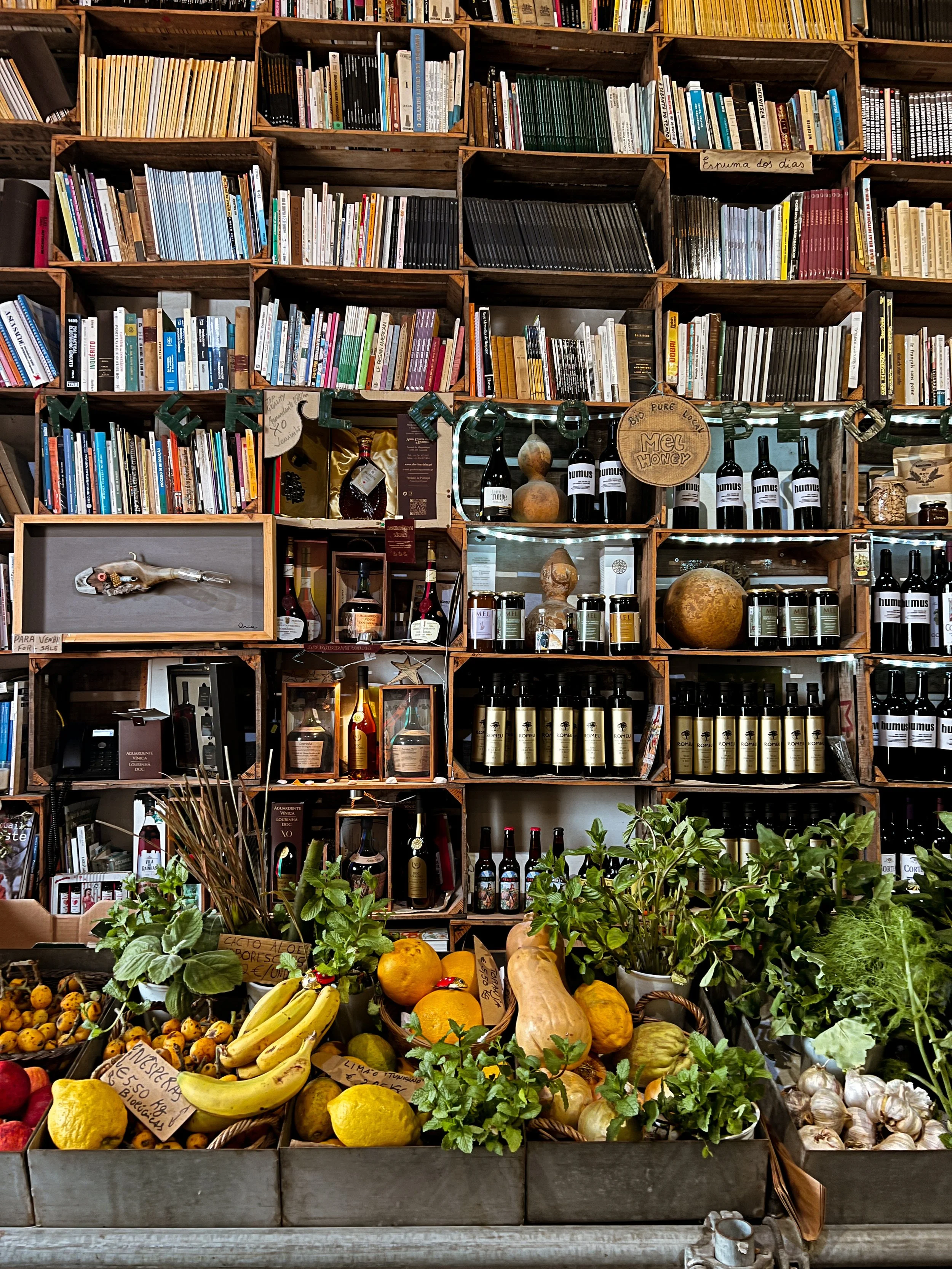 Display of fresh fruits and herbs in front of a wooden shelf filled with books and bottles.