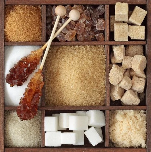 A variety of different types of sugar in a wooden box compartment, including brown, white, raw, and specialty sugars.