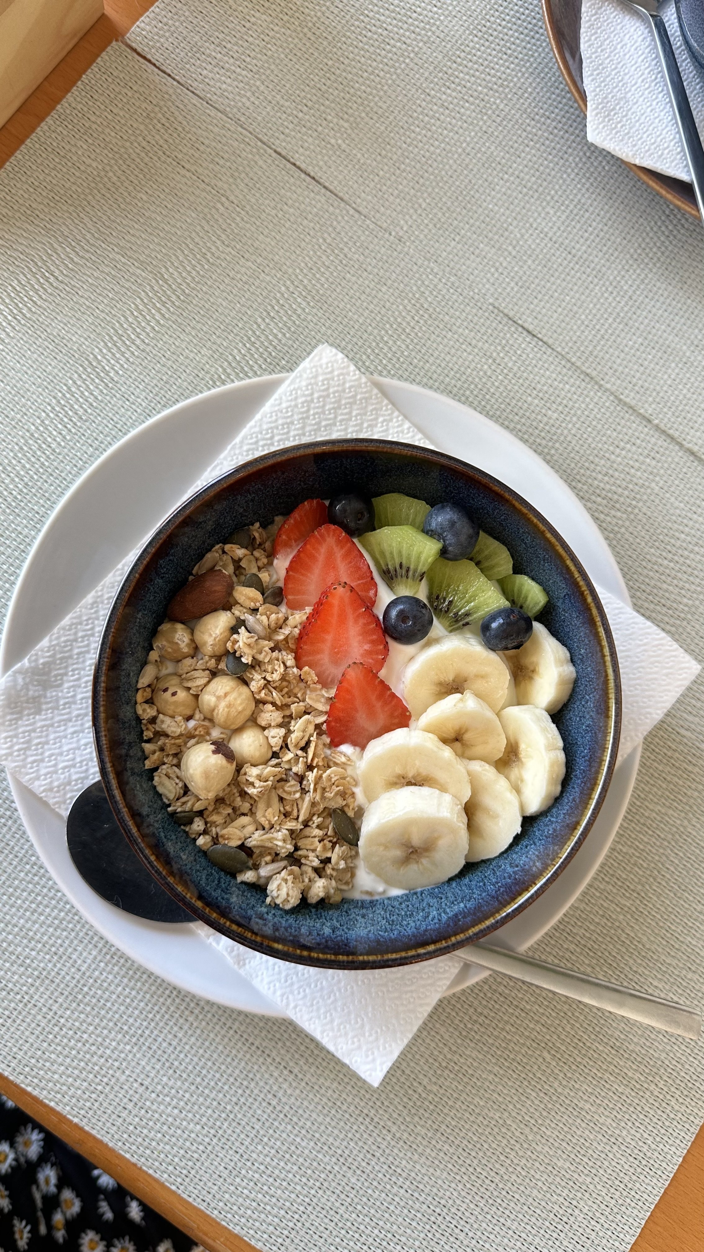 A bowl of yogurt topped with sliced bananas, strawberries, kiwi, blueberries, granola, and nuts.