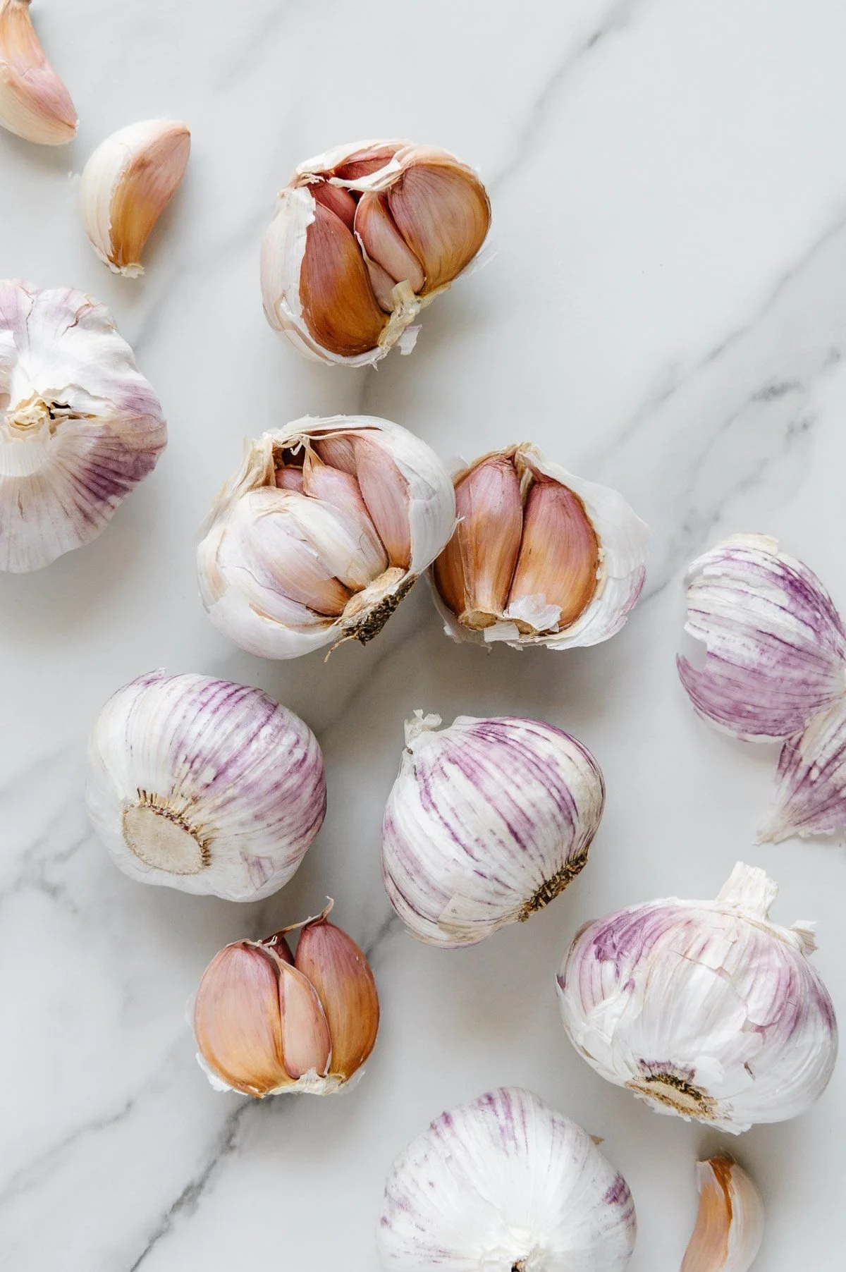 Several garlic bulbs and cloves scattered on a white marble surface.