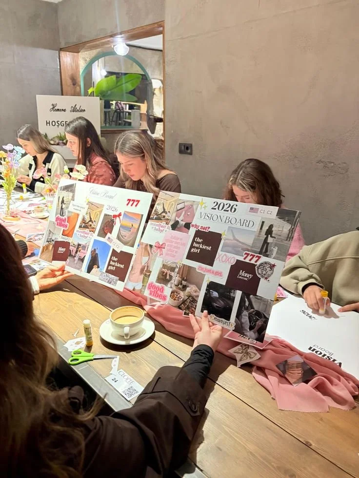 Women sitting at a long table with vision boards and craft supplies during a group activity or workshop.