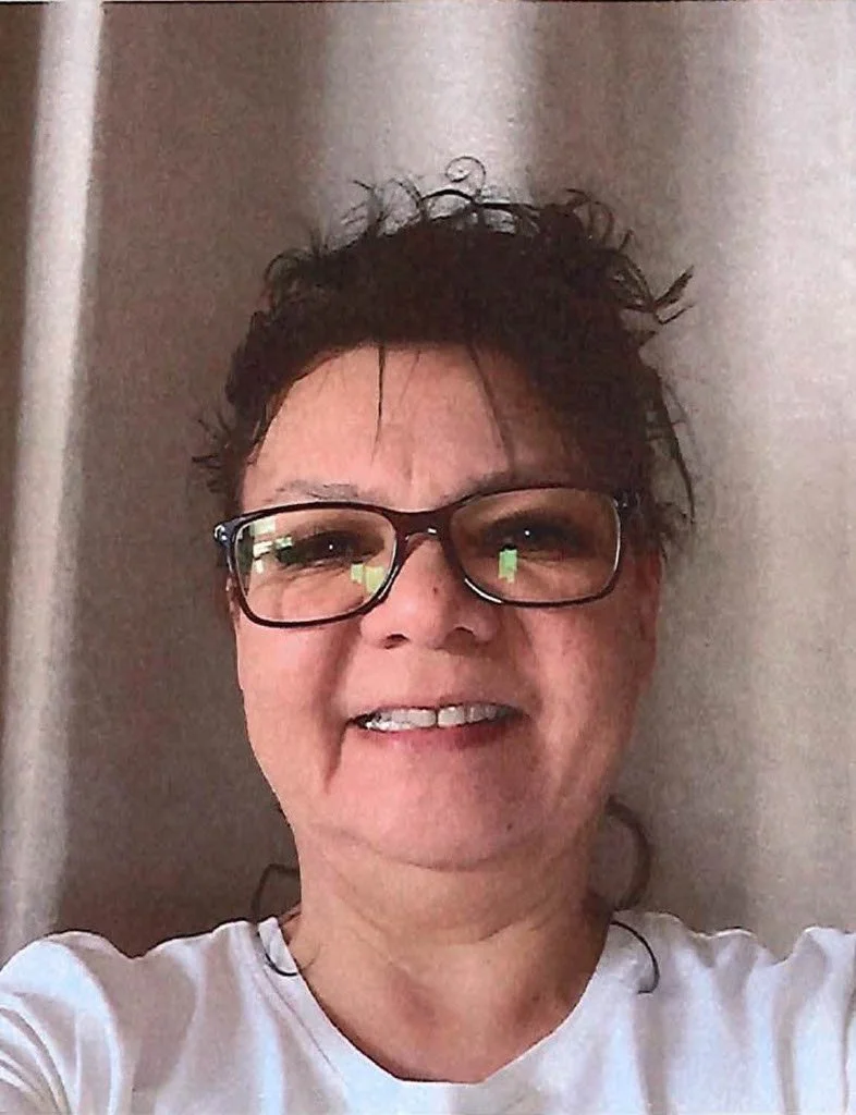 Person wearing glasses and a white shirt smiling in front of a curtain.