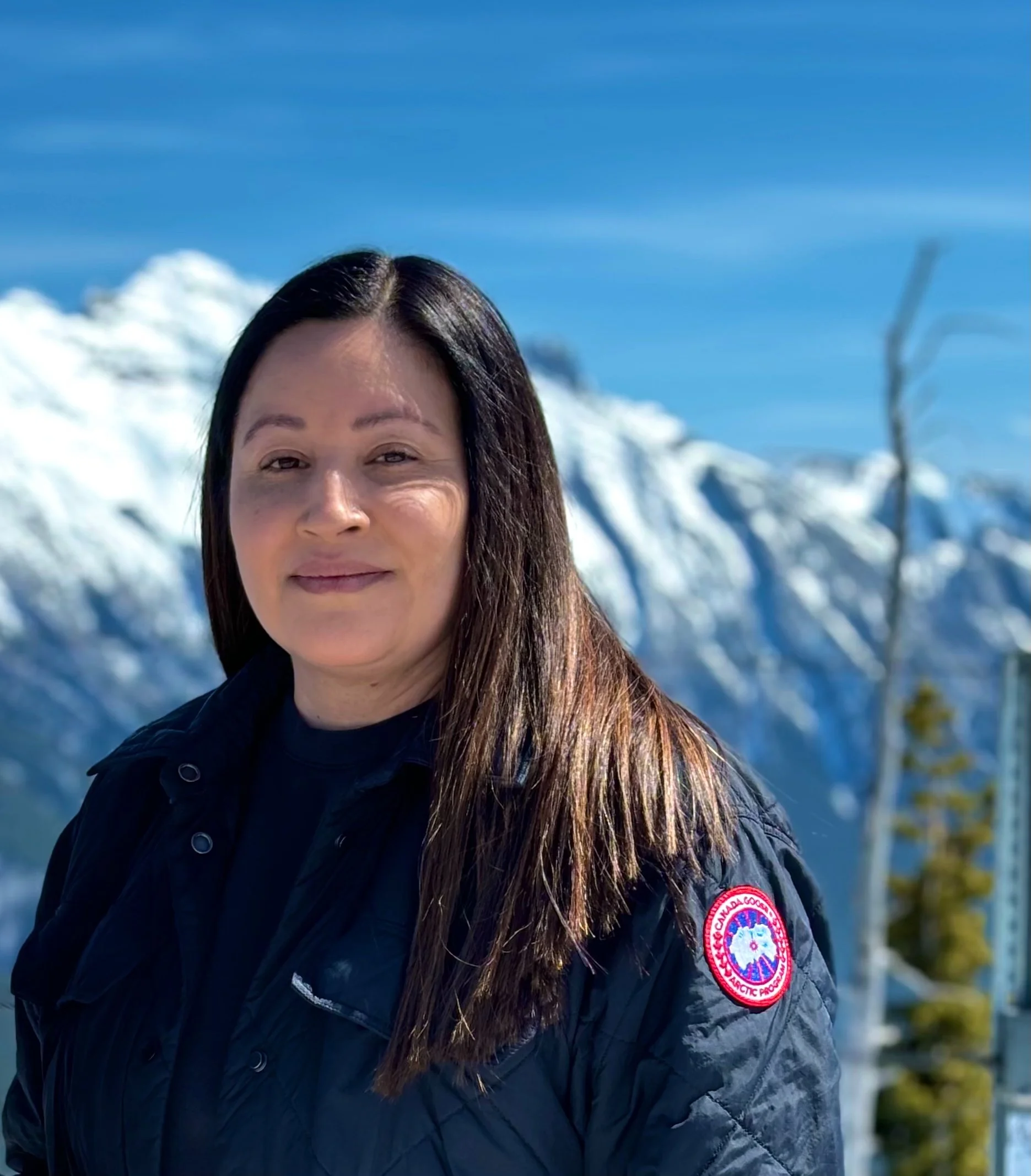 A circular collage divided into four sections, each with a different image. Top left shows people working at a table with sticky notes. Top right features a group sitting outside on grass. Bottom left has a person posing by leafy plants. Bottom right displays a group of people indoors with a laptop.