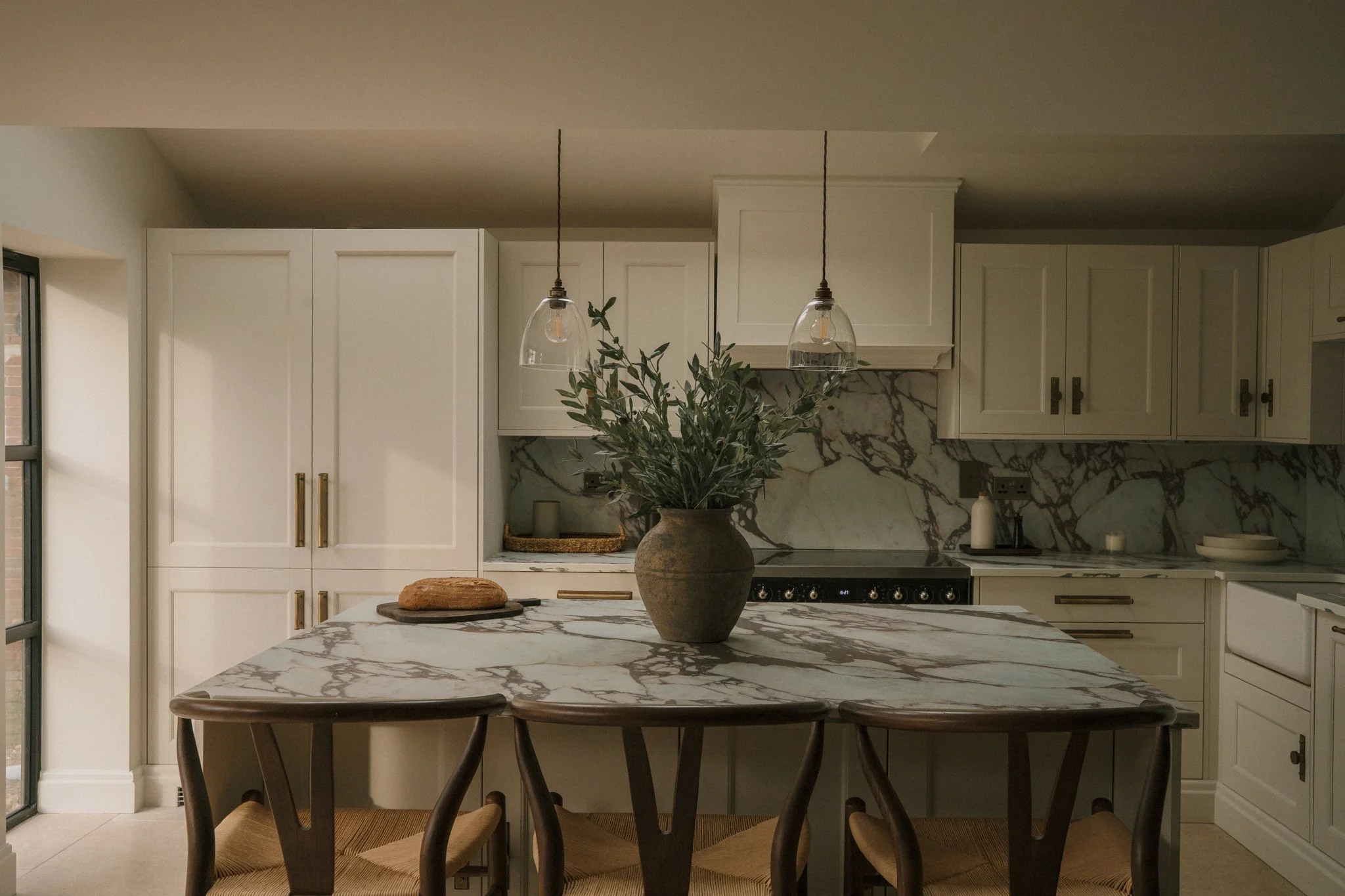 Modern kitchen with white cabinets, large island with wicker-backed stools, pendant lights, and built-in appliances.