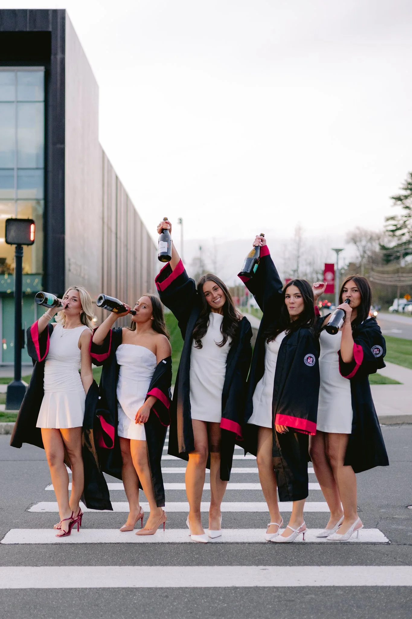 group of girls taking graduation photos at sacred heart university while walking with champagne