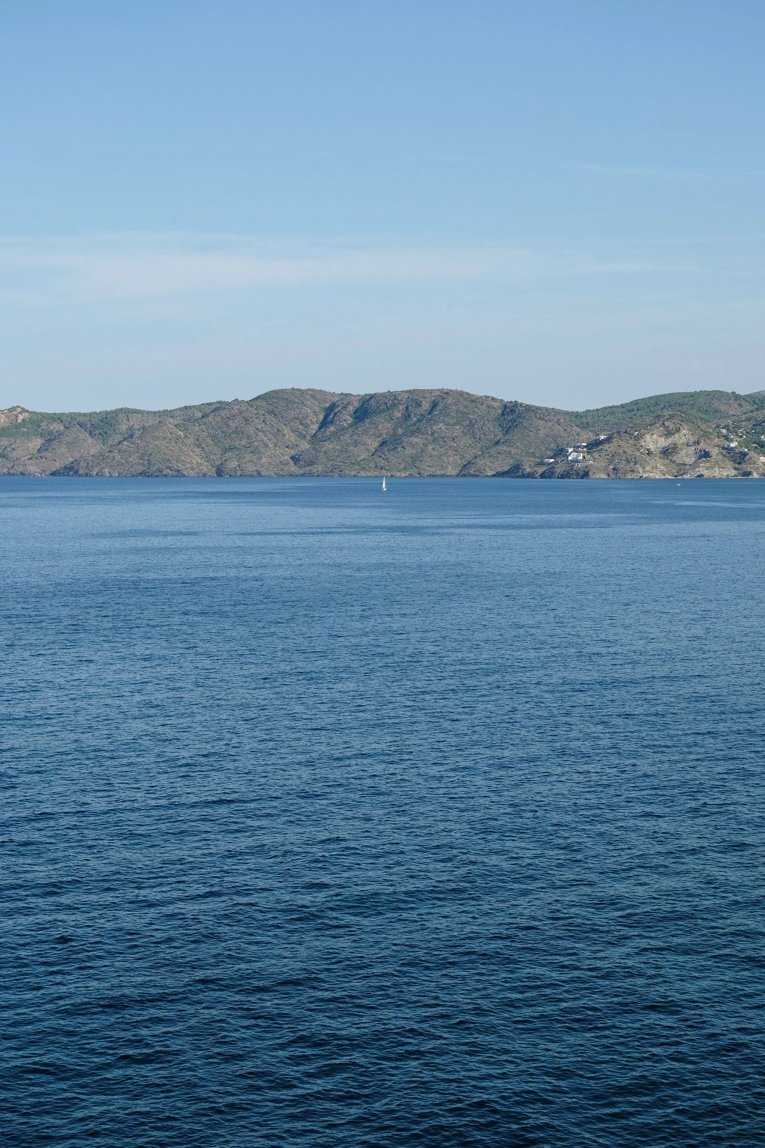View of a lake or sea with blue waters and gentle waves, with a mountain range in the background under a clear sky.
