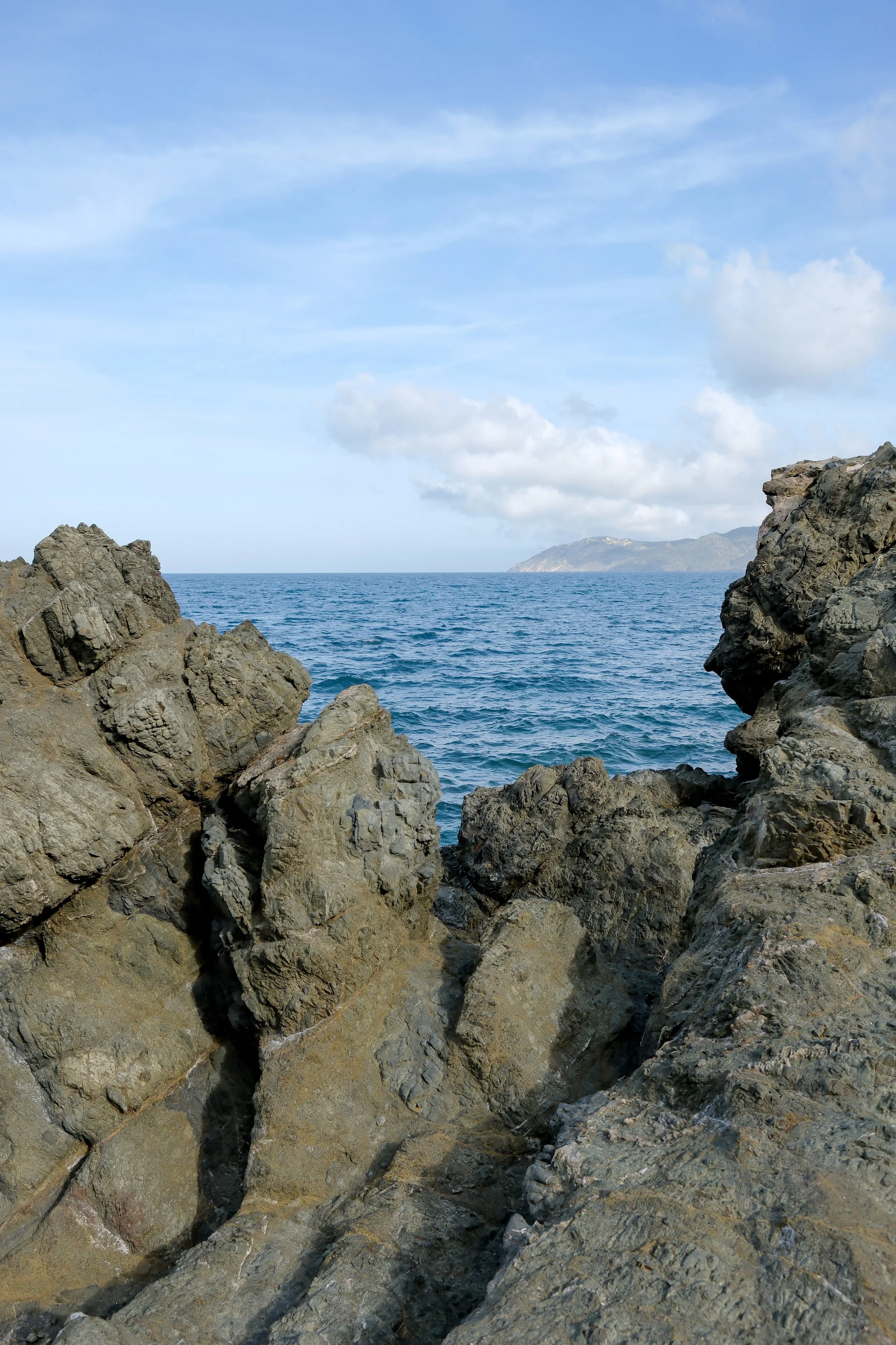 View of the ocean with rocks in the foreground and a partly cloudy sky.