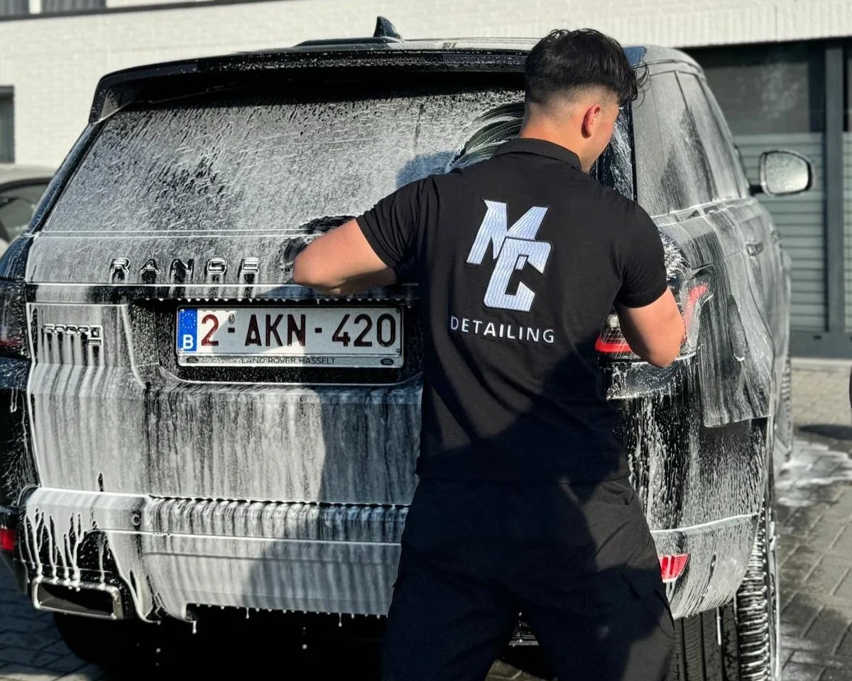 Man wast een zwart SUV met schuurspons en zeep in een carwash.