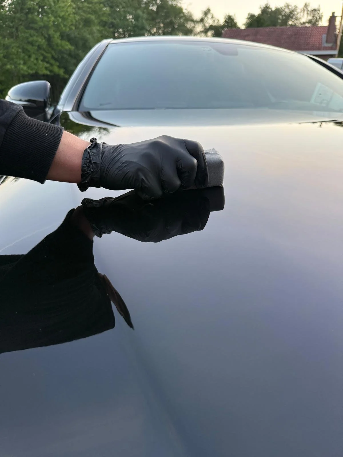 Persoon met zwarte handschoen die de lak van een zwarte auto poetst, met reflectie van de hand en poetsdoek op het oppervlak.