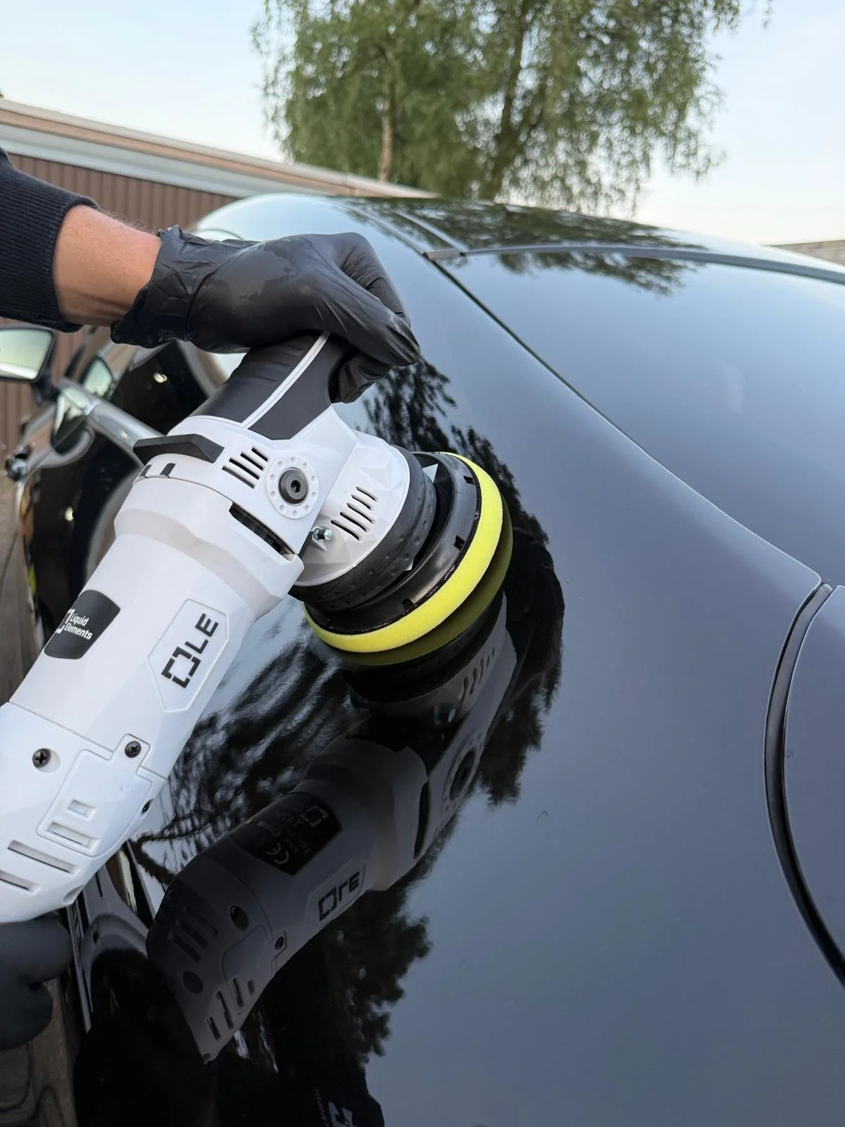 Persoon gebruikt een elektrische polijstmachine op de auto tegen een zwarte auto.