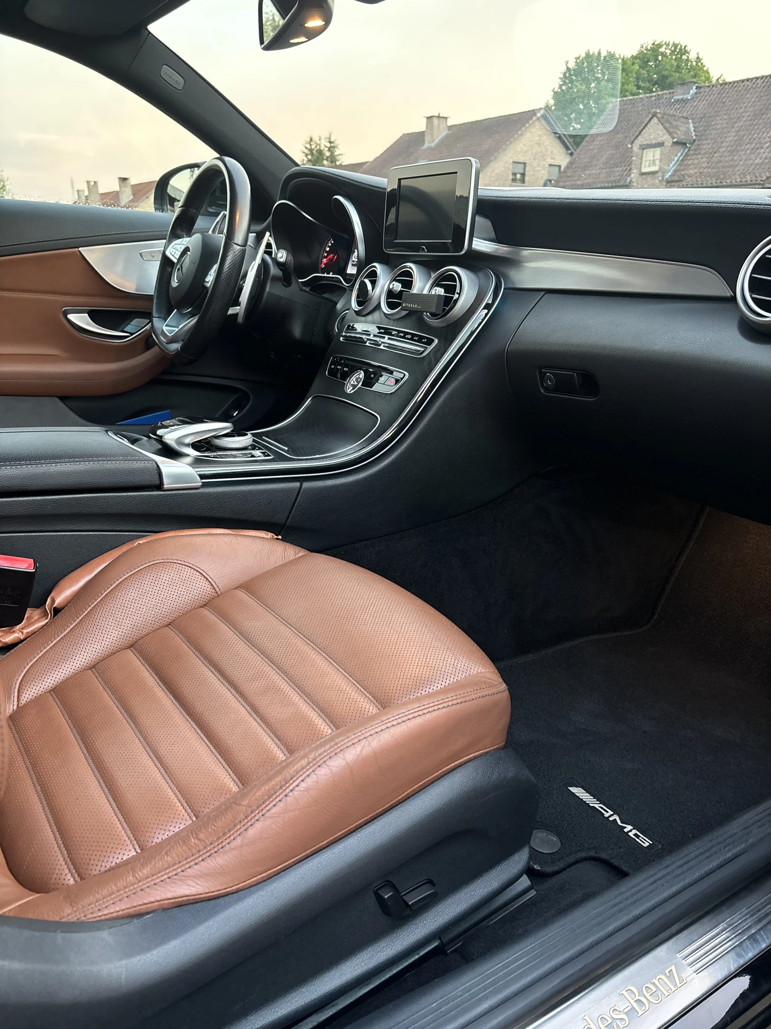 Interieur van een Mercedes-Benz met een bruin lederen stoel, zwart dashboard, en een ingebouwde entertainmentmonitor.