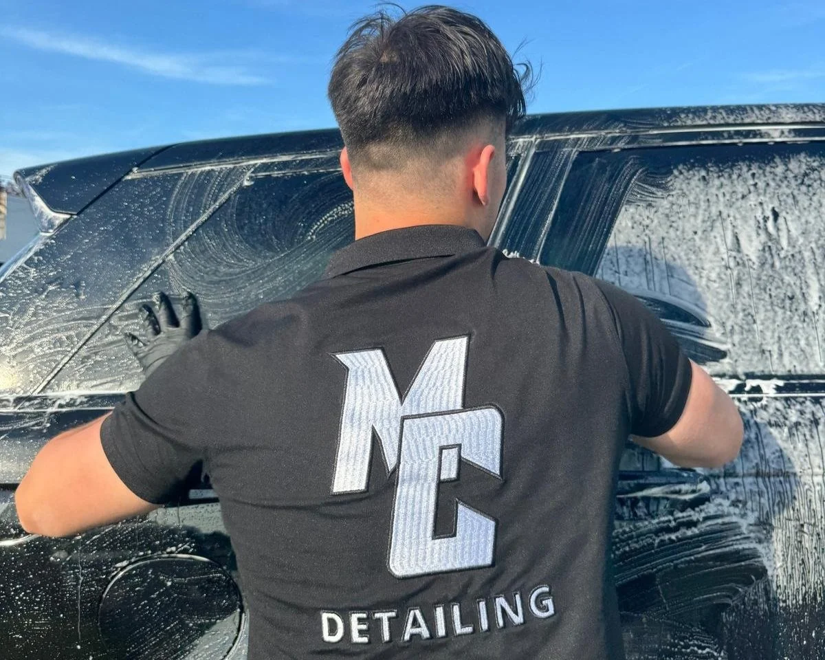 Man die de ruiten van een zwarte auto schoonmaakt met zeem en water.
