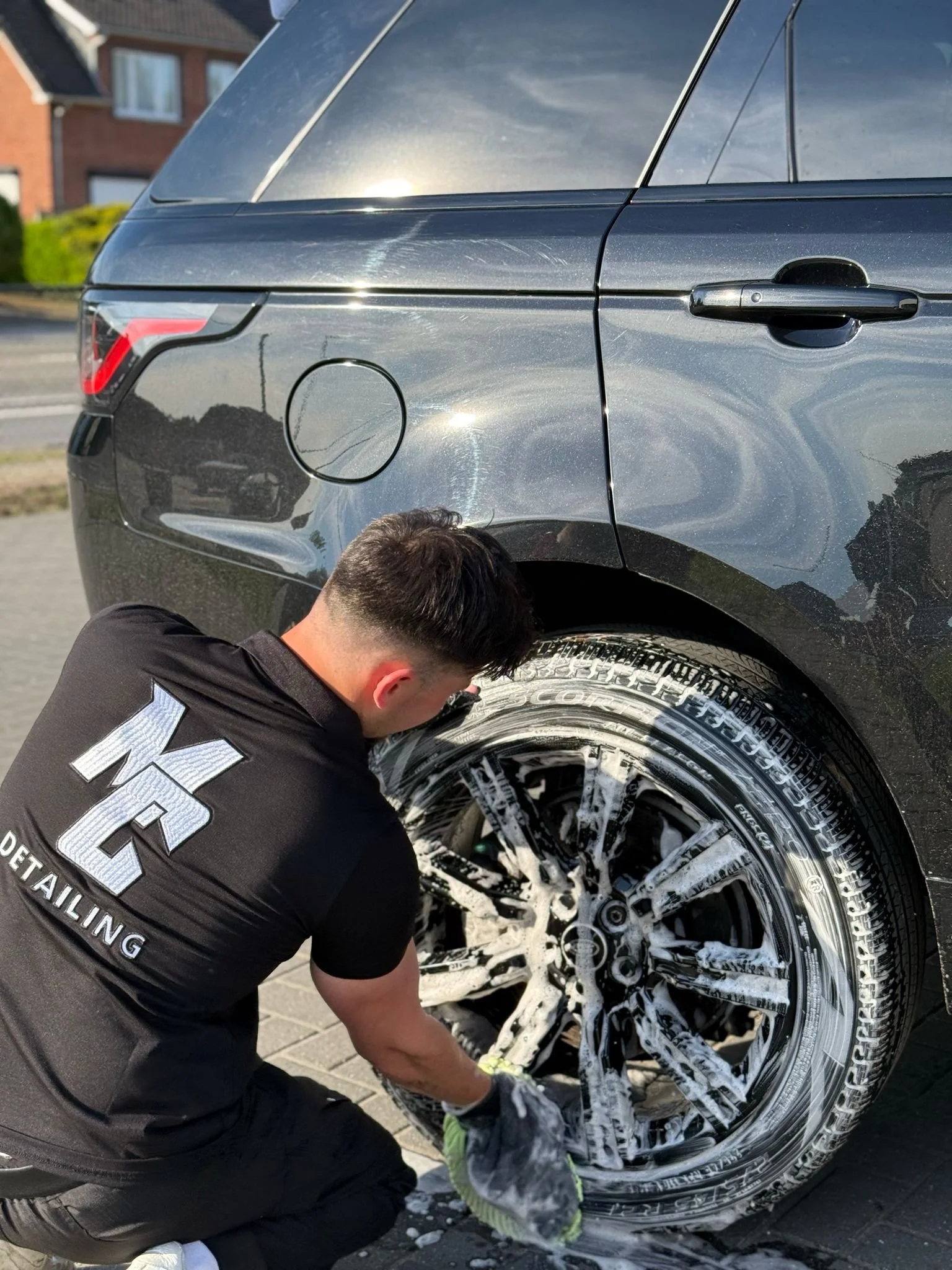 Man wast een zwarte auto met zeep en borstel, banden worden schoongemaakt