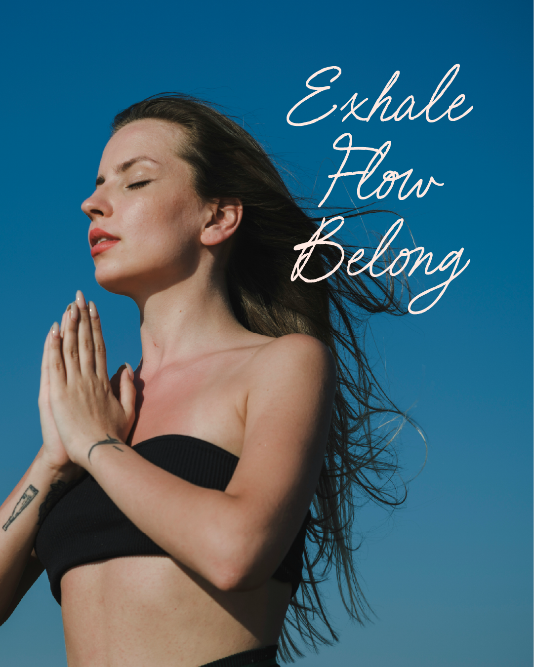 A woman with closed eyes and hands in a prayer position outdoors against a blue sky, with the text 'Exhale, Flow, Belong' written in white script.
