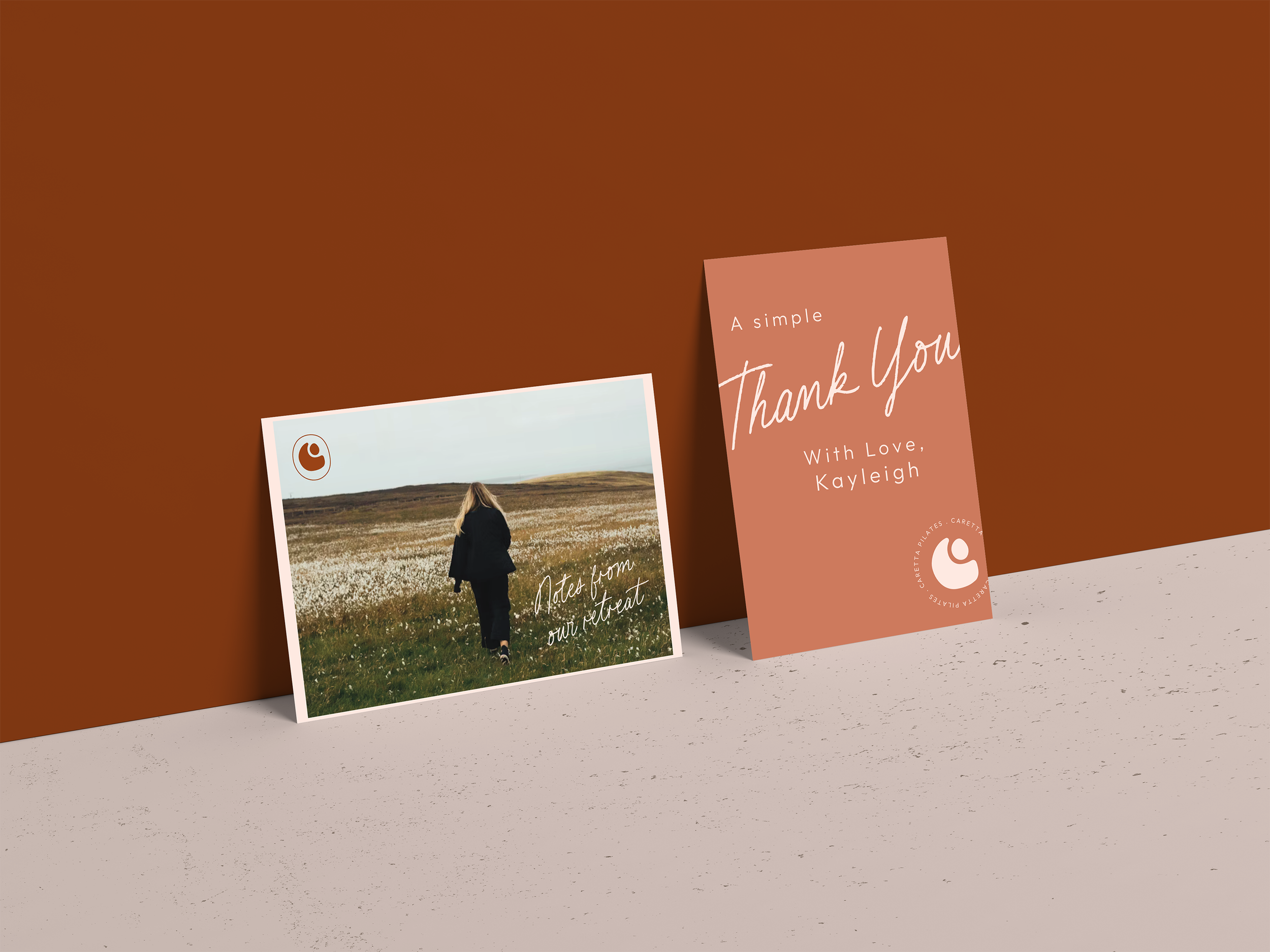 A thank you card and a note card displayed against a brown and beige background. The thank you card is pink with white script text that says 'A simple Thank You with Love, Kayleigh' and has a logo in the bottom right corner. The note card features a person walking in a grassy field with white flowers under a cloudy sky, with handwritten-style text that says 'Notes from our retreat' and the same logo in the corner.